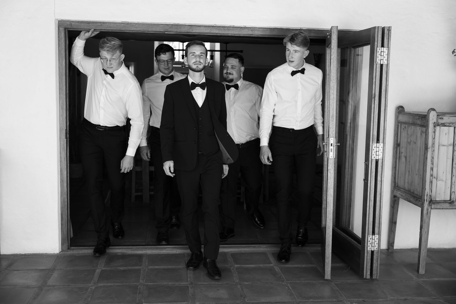 People in formal attire walking through a doorway in black and white photography.