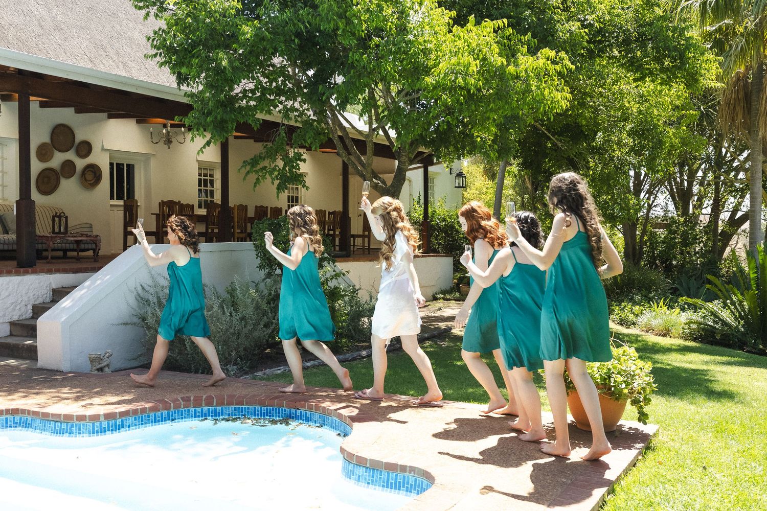 A panoramic view of people enjoying activities by a swimming pool in a sunny backyard garden.