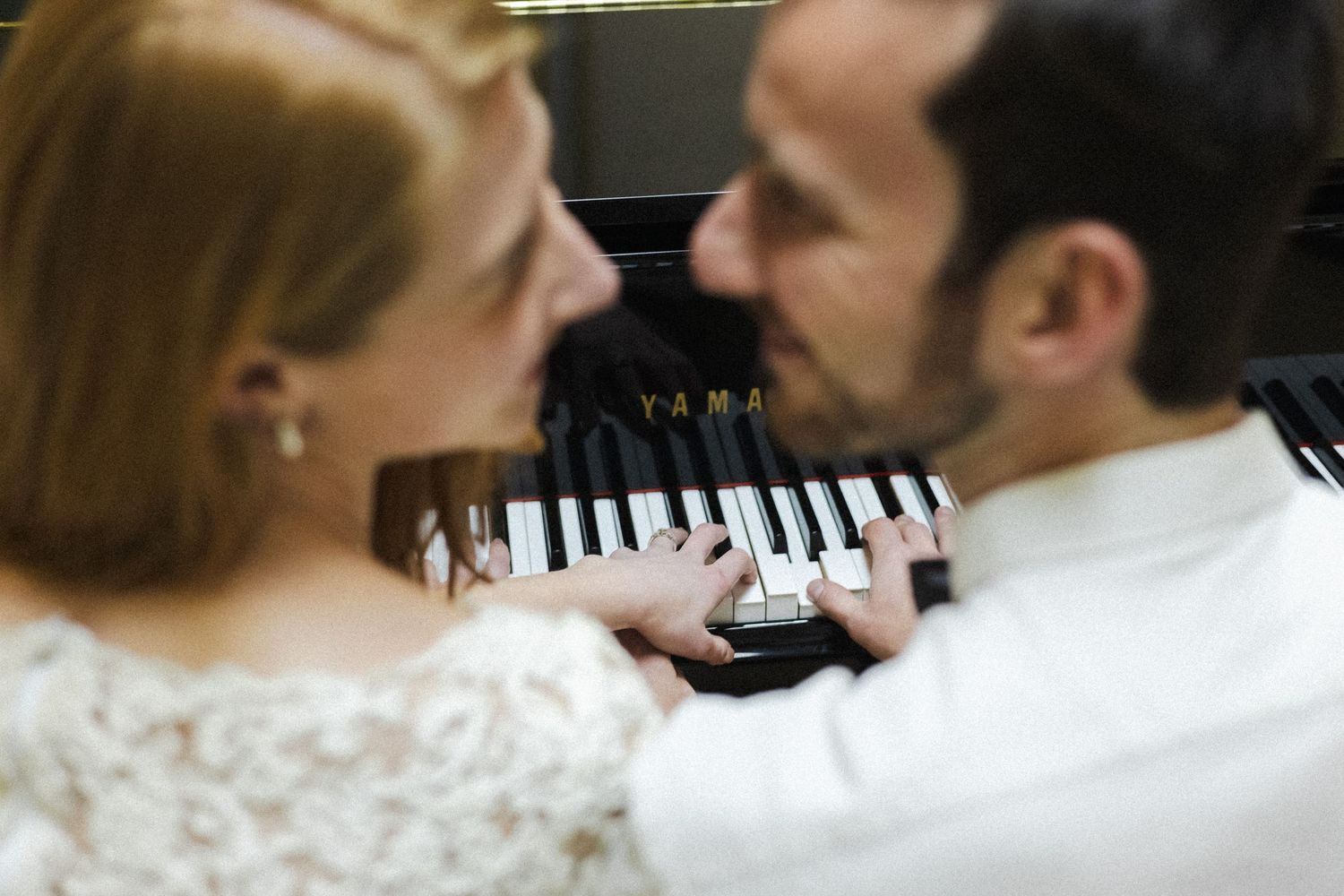 A couple shares a romantic moment while playing piano together in formal wedding attire.
