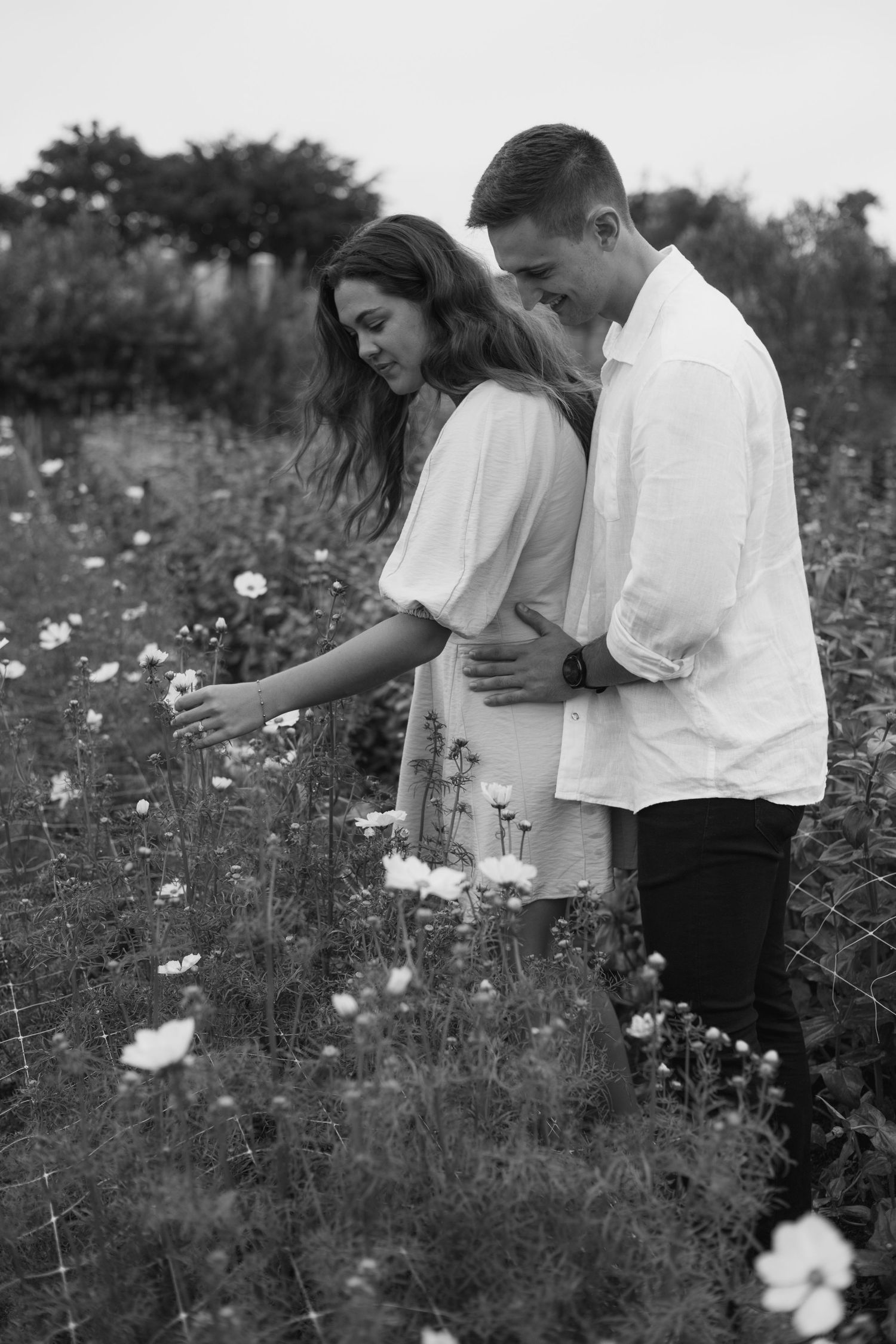 Black and white photo of couple sharing intimate moment among wildflowers.