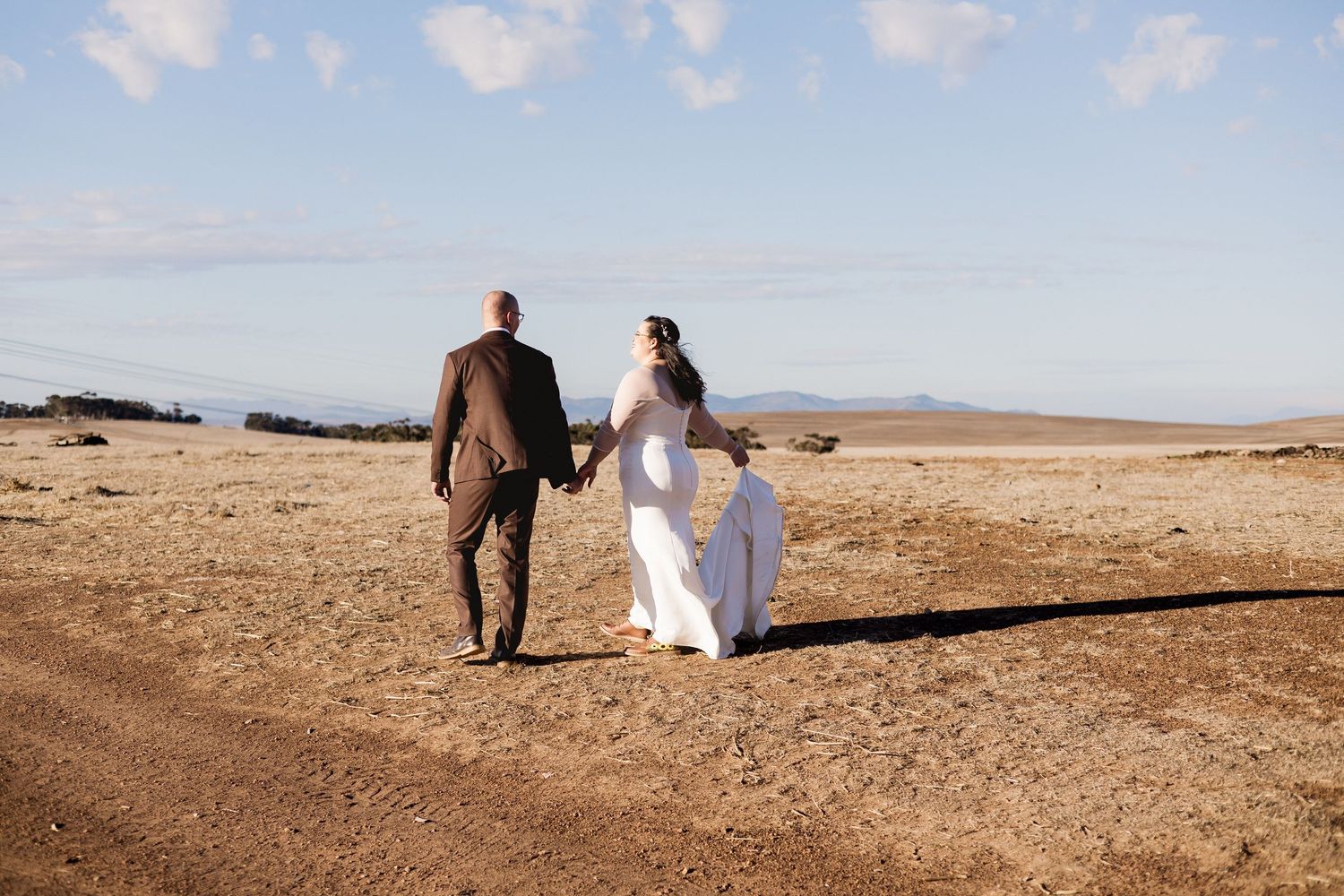 Bride and groom walking hand in hand through an arid landscape on their wedding day.