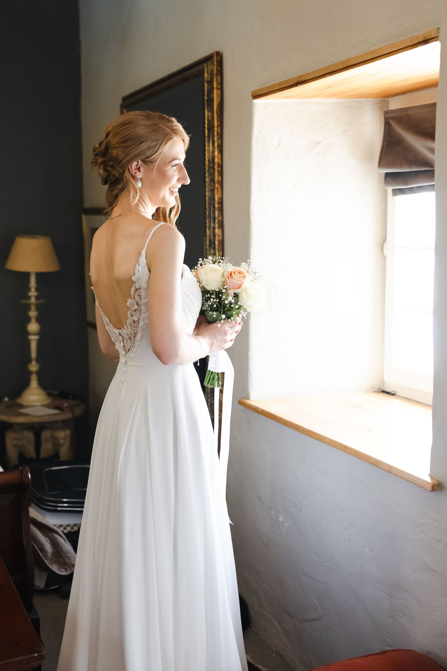 A flowing white wedding gown photographed in natural window light against neutral walls.