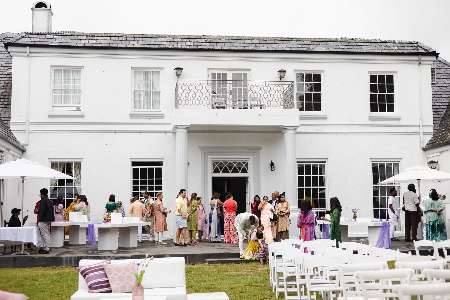 White Georgian mansion with colorful dresses displayed on hangers along the exterior wall during a summer event.