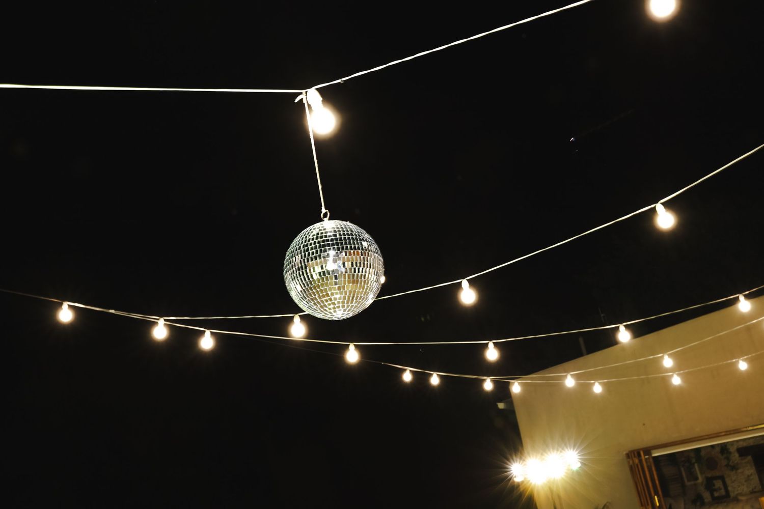 String lights and a disco ball create a festive ambiance against a dark ceiling at an indoor party venue.
