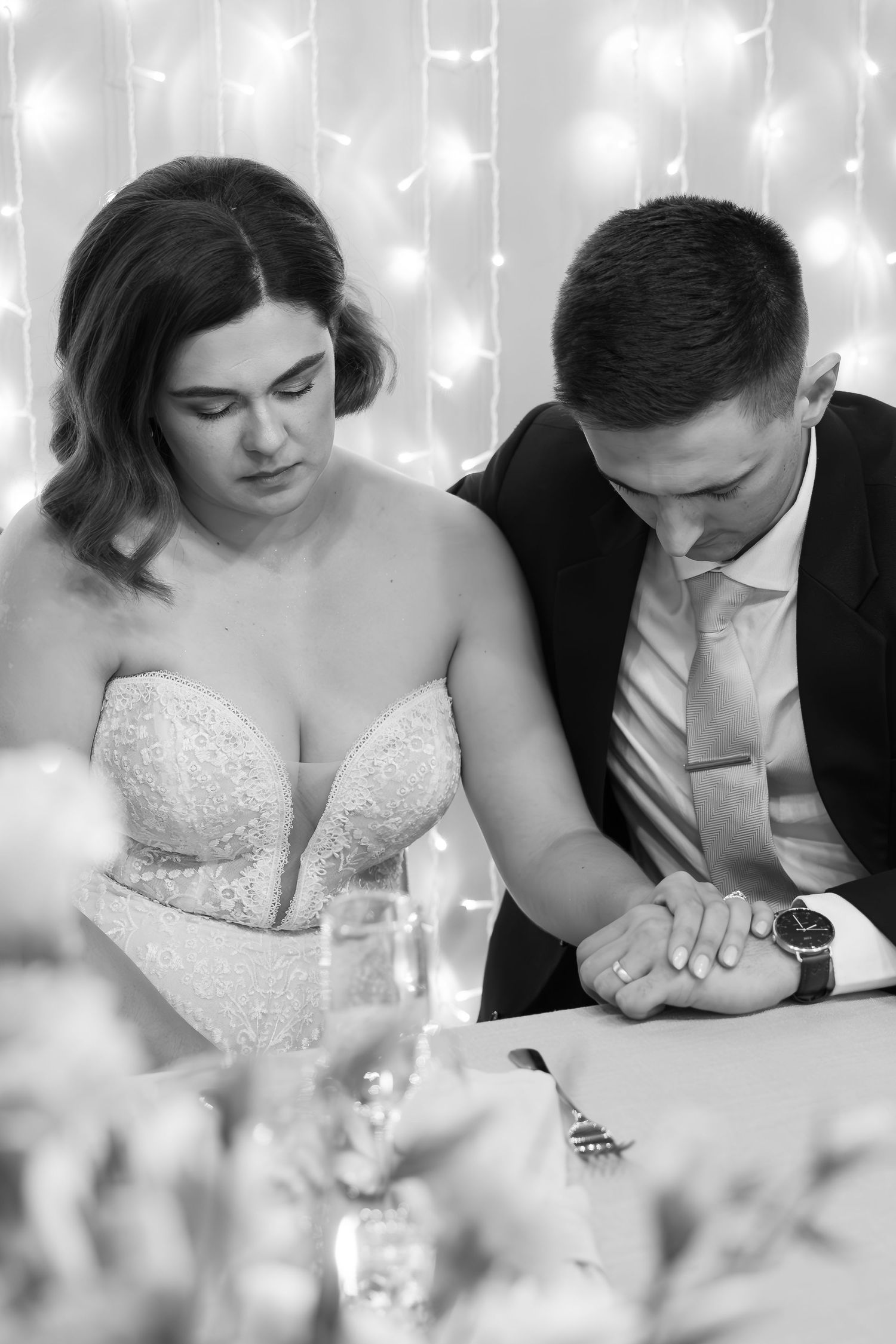 Black and white wedding reception photo sequence showing couple looking down at table during emotional moment.