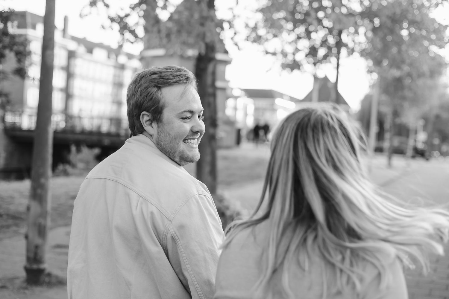 Black and white photo of a smiling man and a woman with flowing hair enjoying a moment together outdoors.