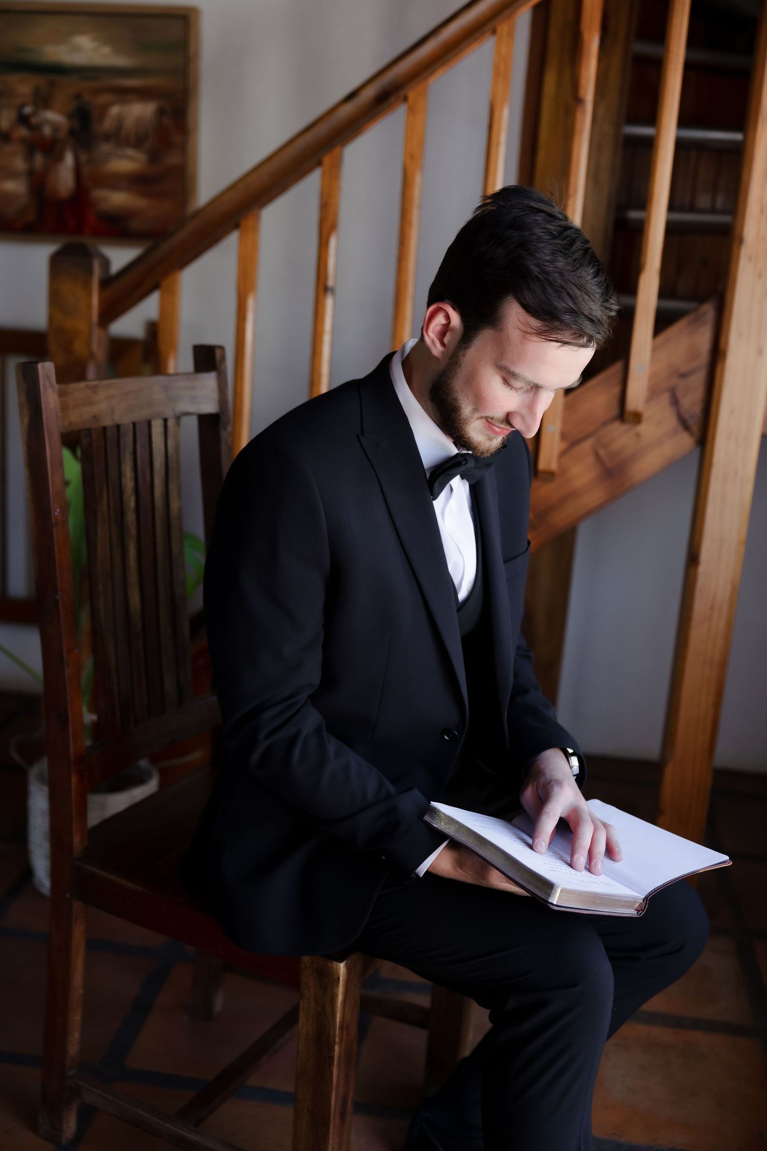 Multiple views of someone in a black suit reading while seated near a wooden staircase.