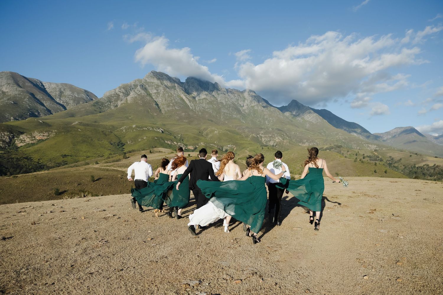 A panoramic sequence showing paragliders preparing and launching from a mountain slope against a blue sky and rugged peaks.