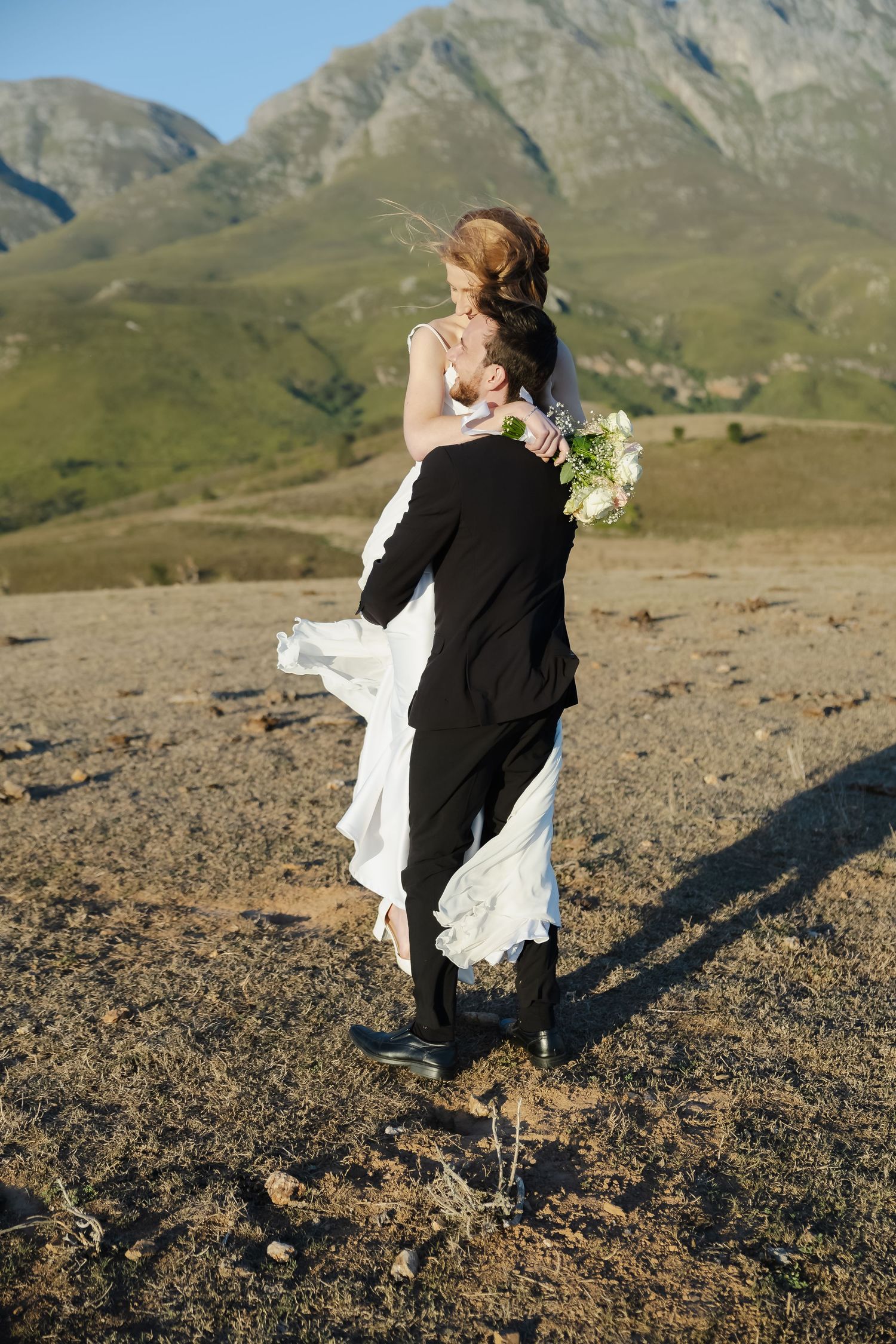 A romantic moment captured against a mountainous backdrop with dramatic rocky peaks and sunlit terrain.
