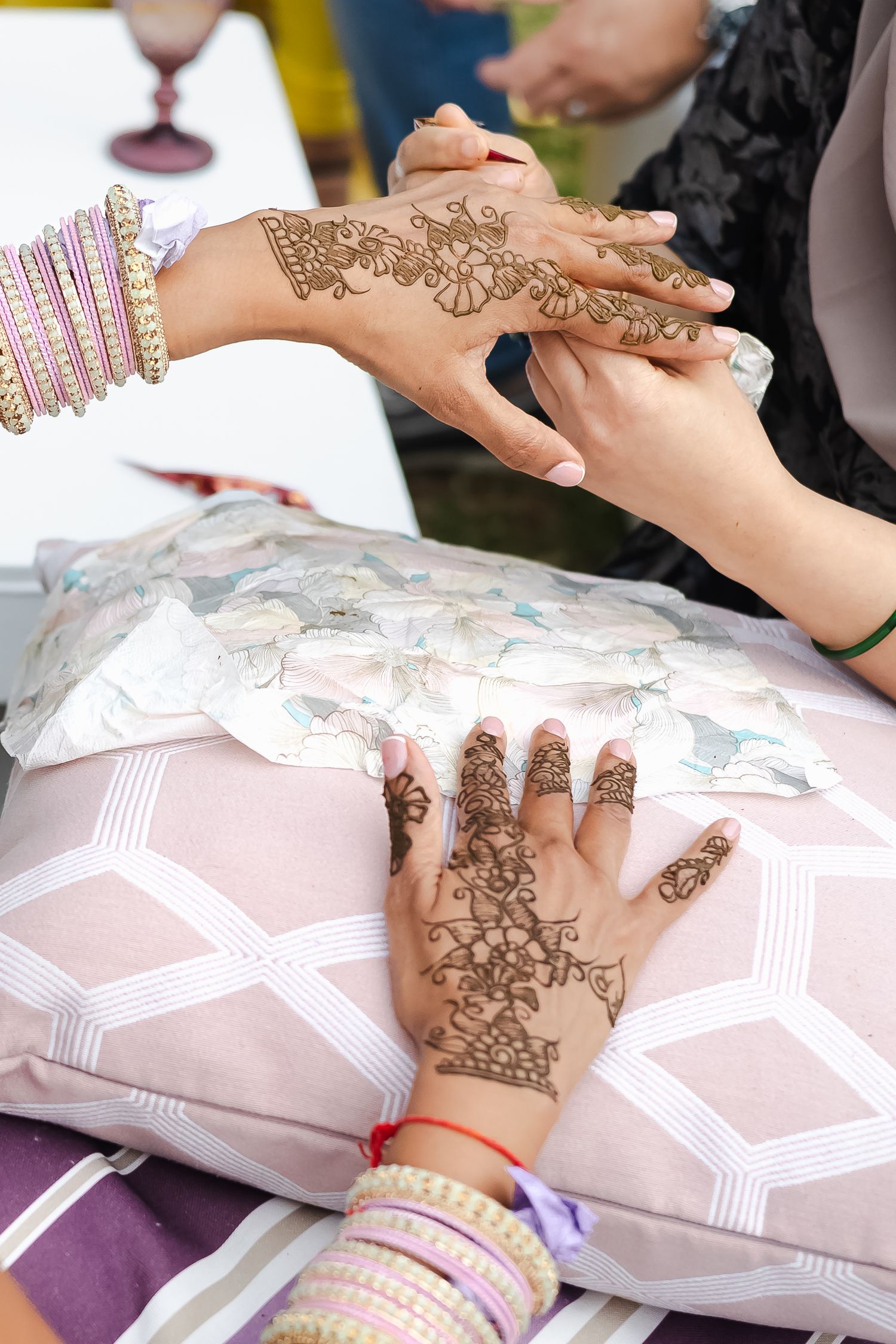 Traditional henna mehndi design being applied to hands with intricate floral patterns over decorative pillows.