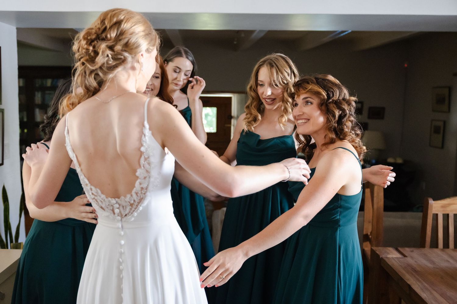 Bride in lace back dress shares special moment with bridesmaids in teal gowns.