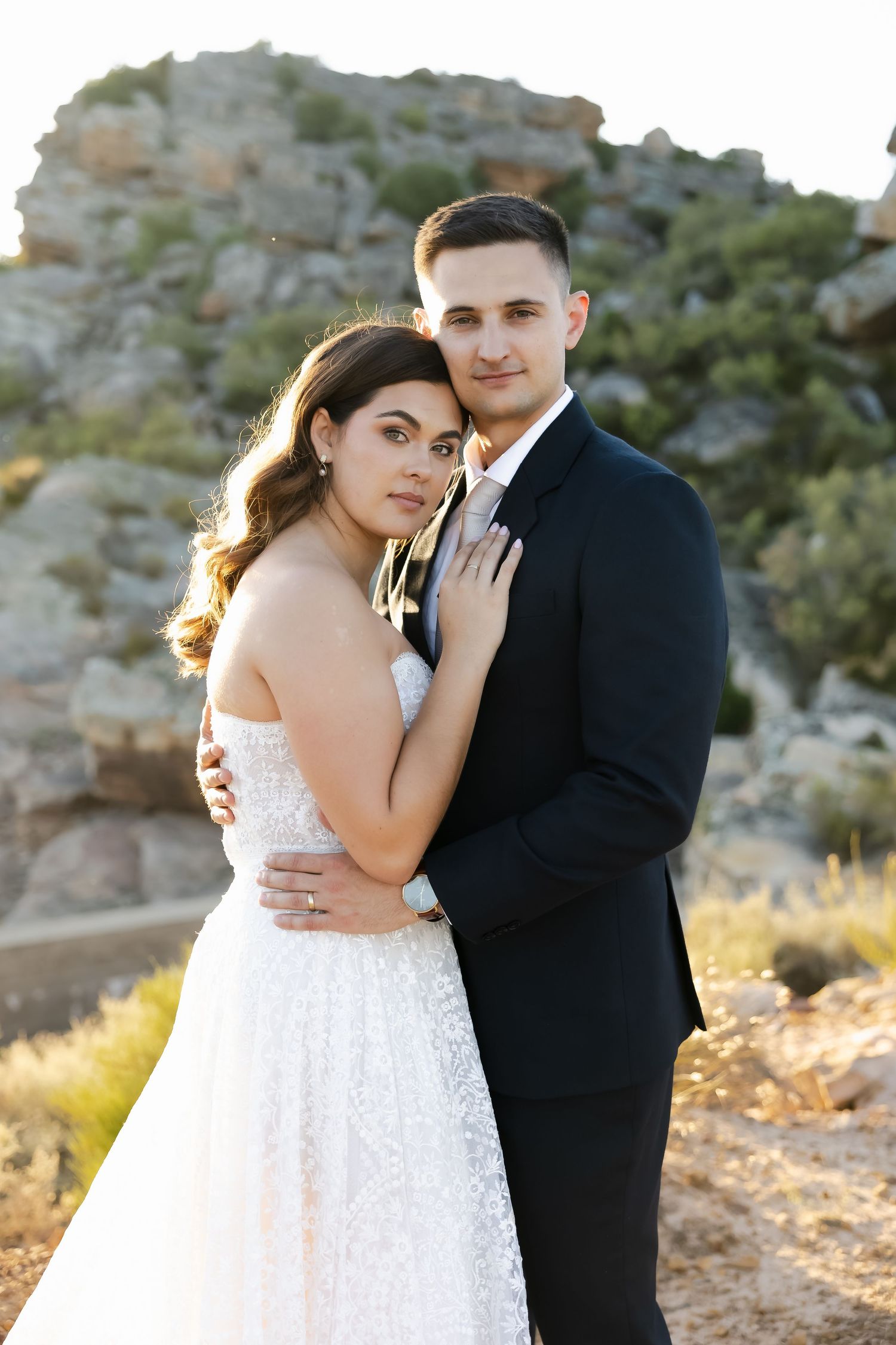 A couple shares an intimate moment outdoors against a rocky mountain backdrop at sunset.