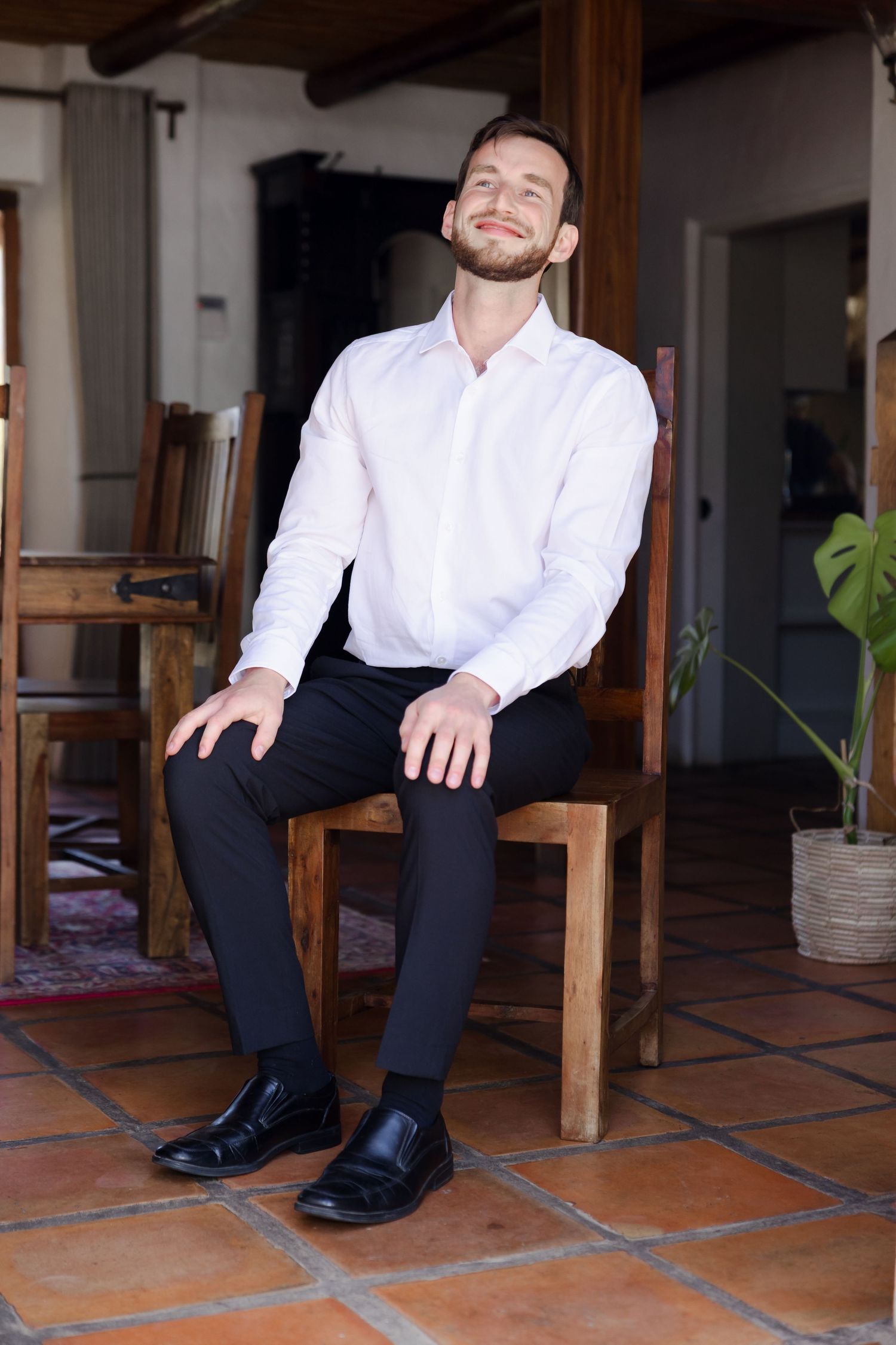 Person in white shirt and black pants sitting on terracotta tile floor in a rustic interior.