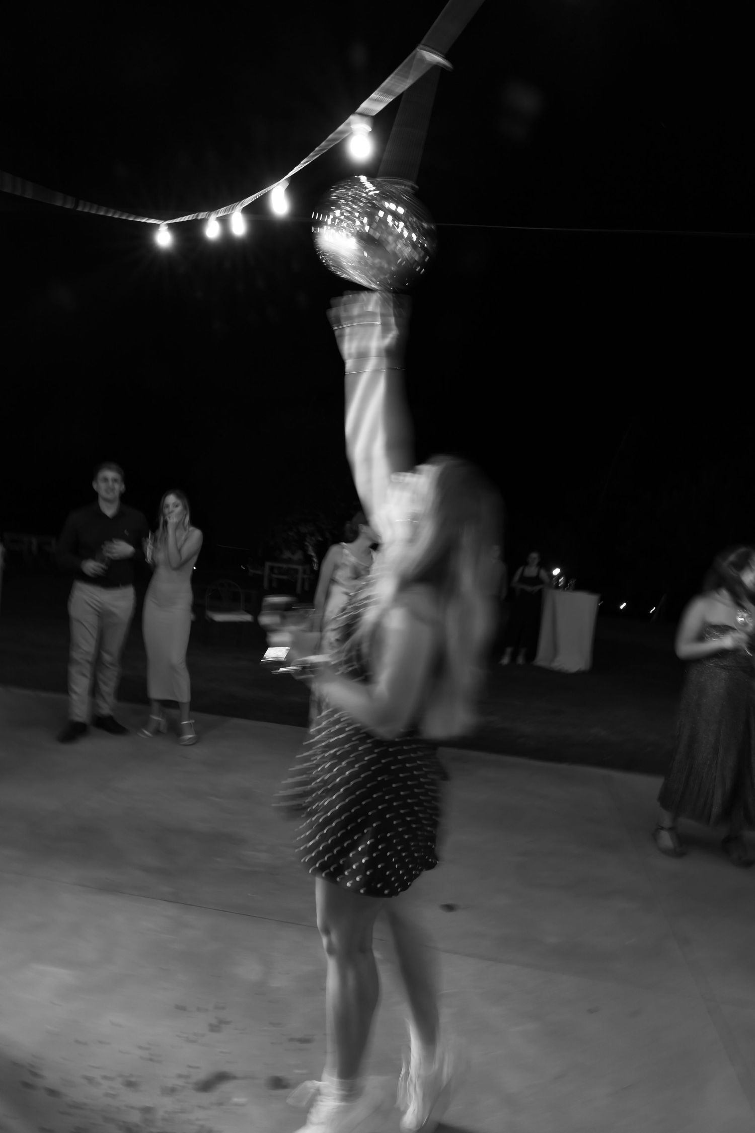 Black and white image of someone dancing beneath string lights at a nighttime event.