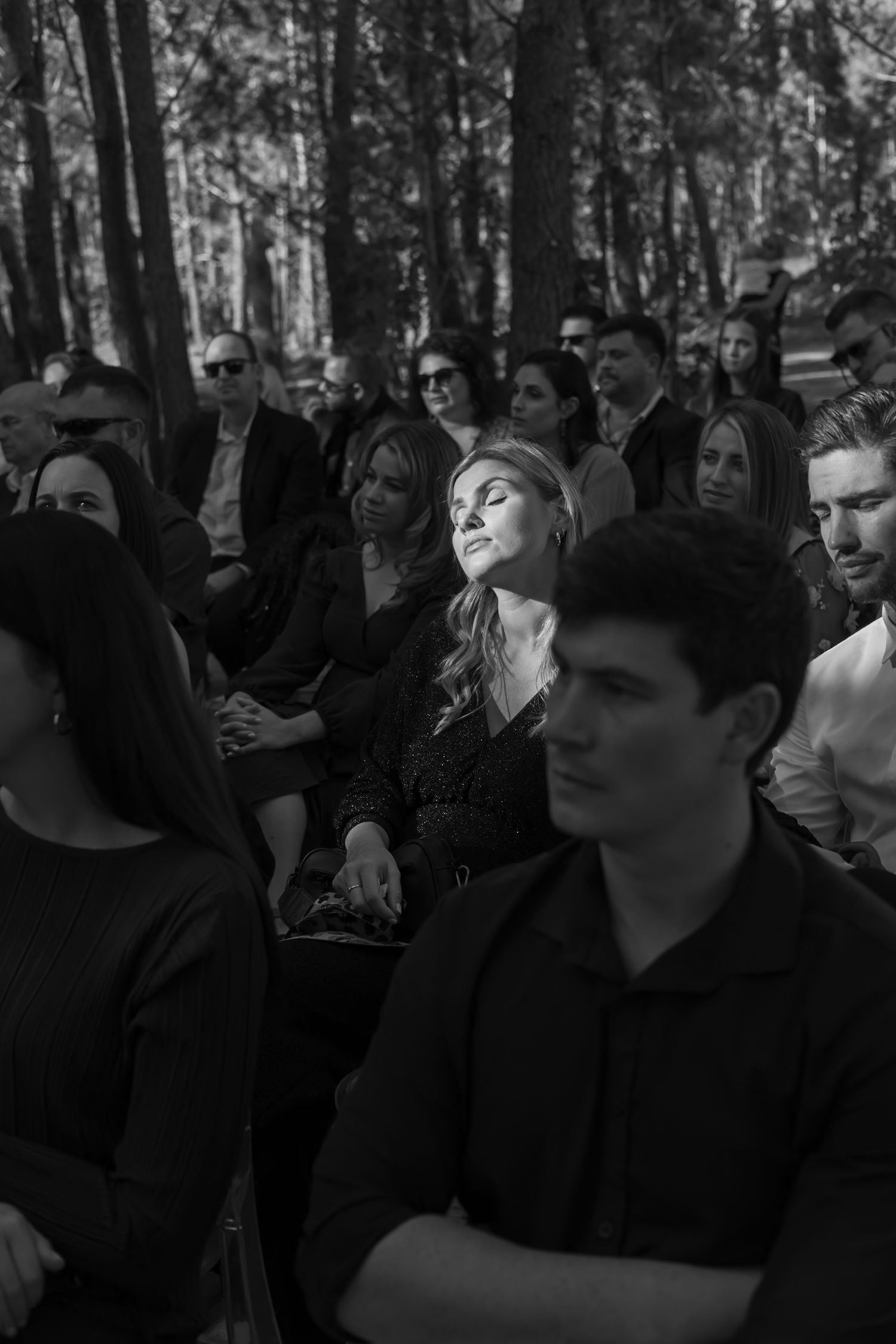 A crowd of people gathered outdoors in a wooded area, shot in black and white.