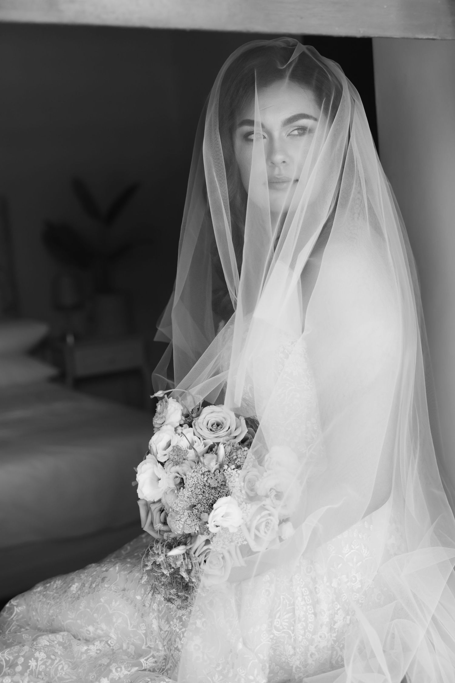 Black and white portrait of a bride in a delicate veil holding a romantic bouquet of roses and flowers.