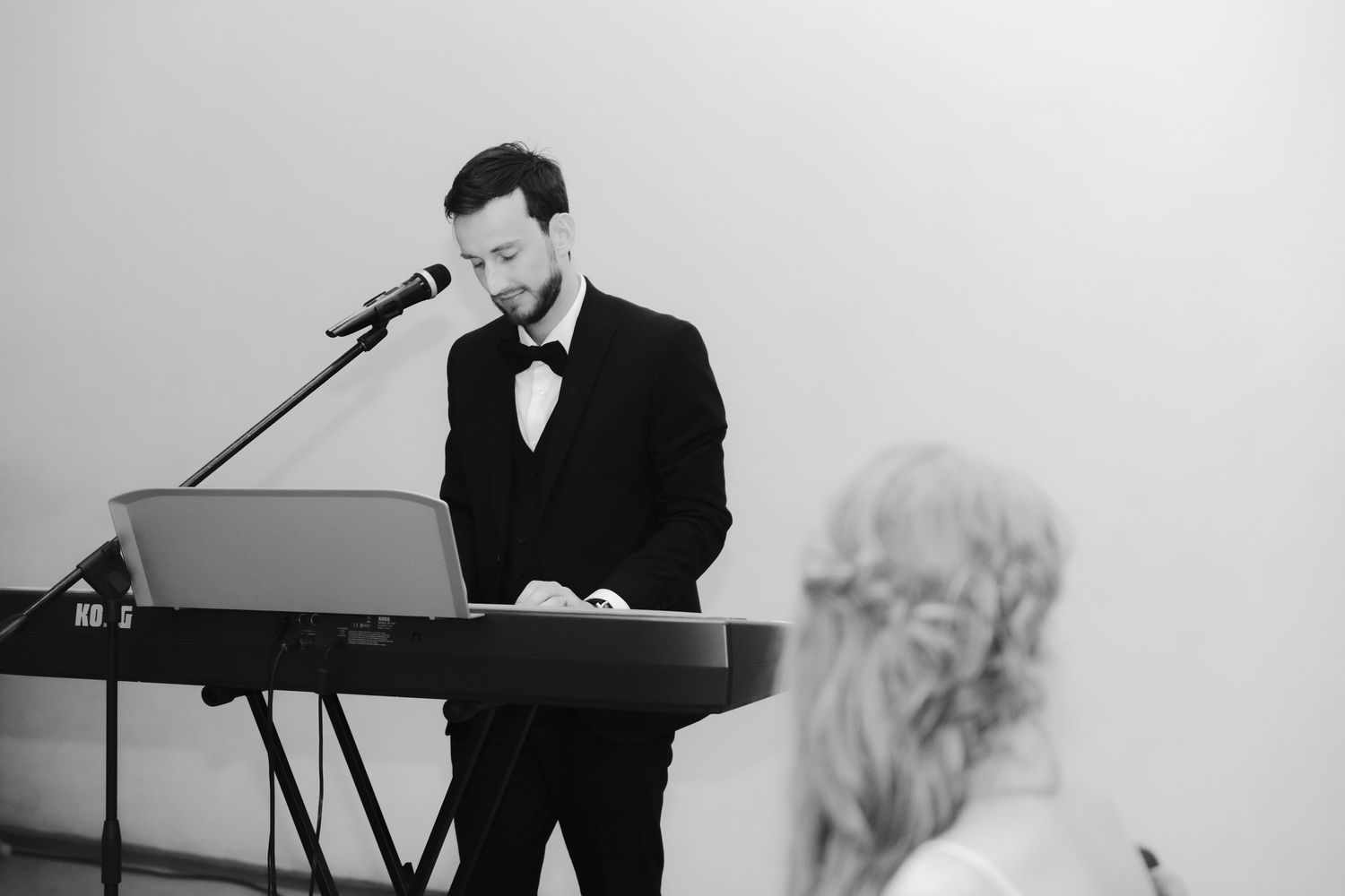 Black and white photo of a musician performing at a piano keyboard during a live performance.