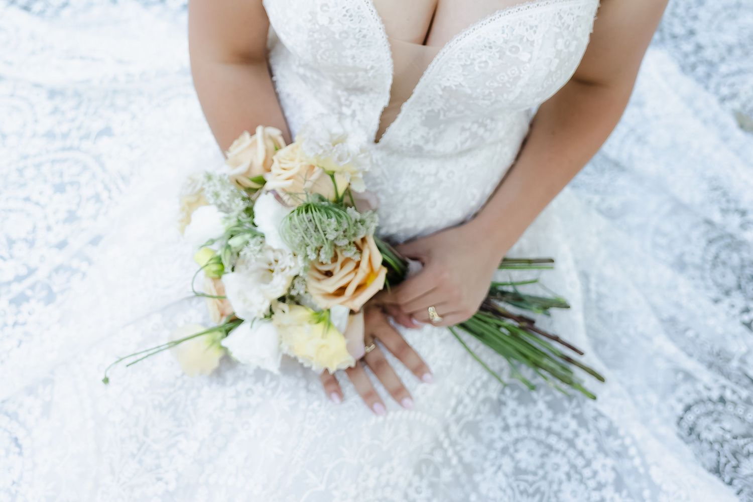 A delicate bridal bouquet with peach roses and succulents rests on a white lace wedding dress.