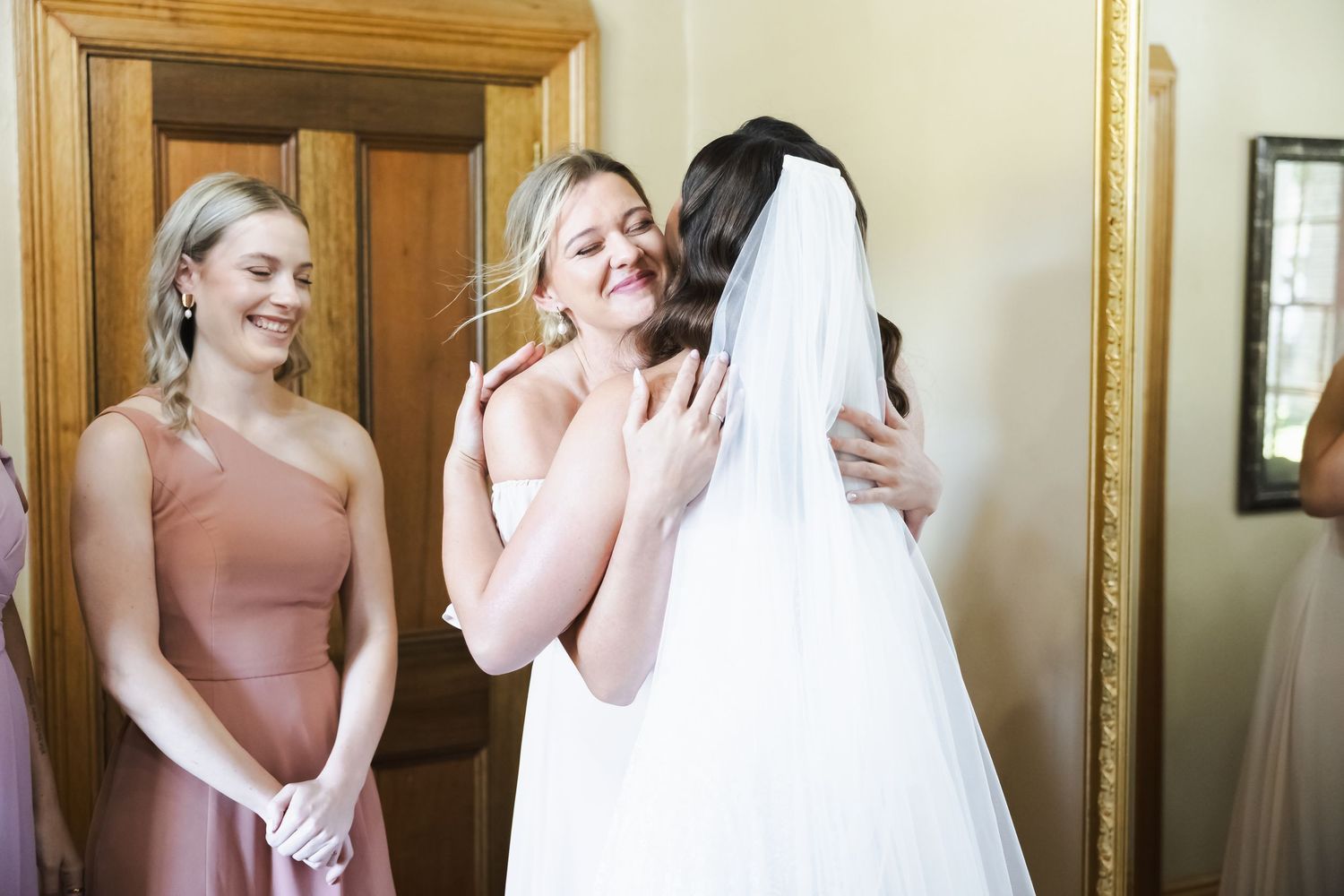 Bridal party members share emotional reactions and laughter while getting ready in a wood-paneled room.