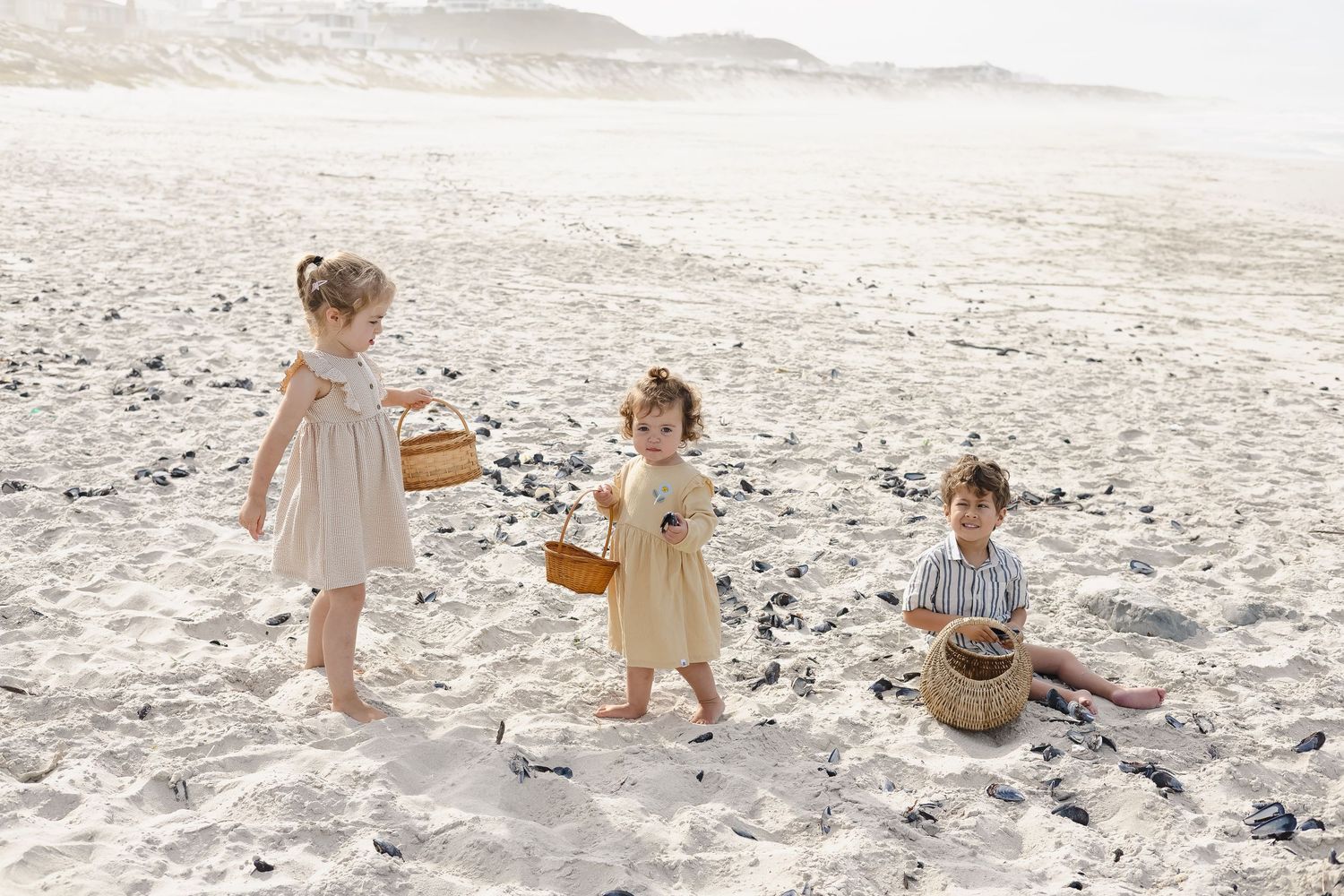 Children playing together on a white sandy beach with baskets and toys on a sunny day.