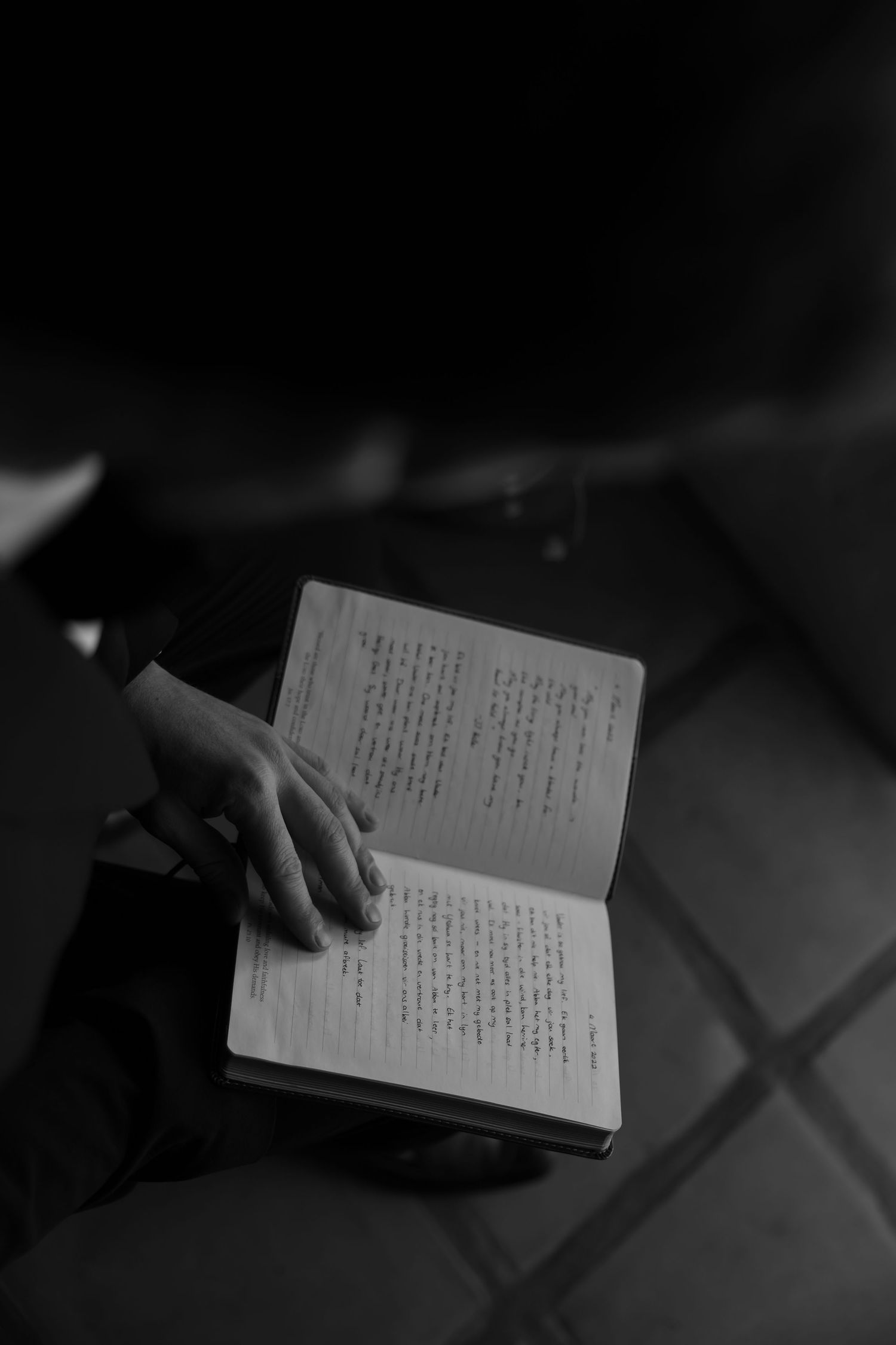 Hand rests on open book with Japanese text in dramatic black and white lighting.