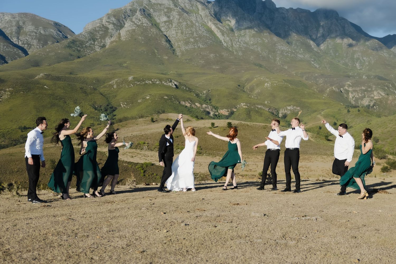 A panoramic sequence shows people lying down on a grassy mountain slope in a domino-style formation against scenic peaks.