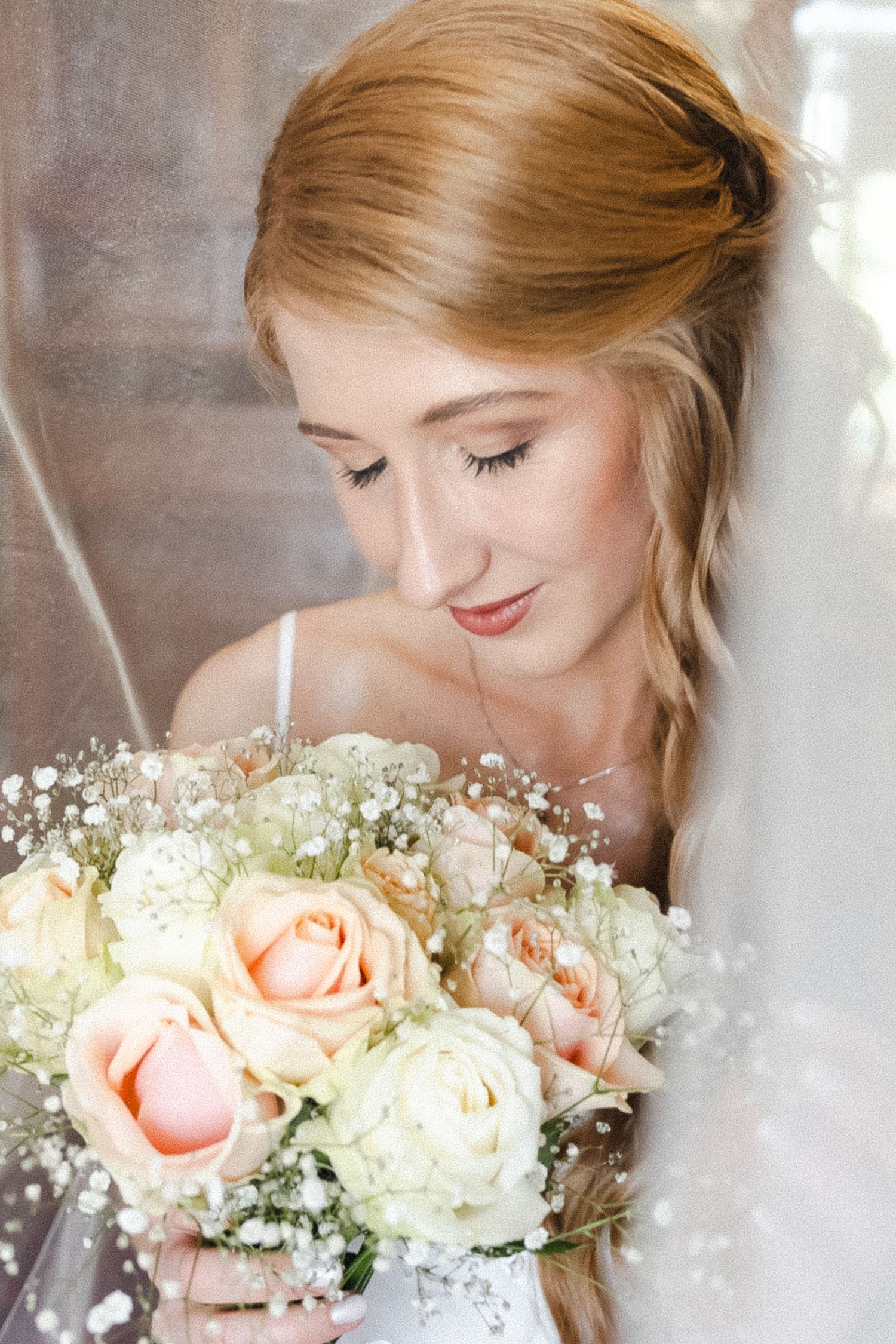 Bride holding delicate bouquet of peach roses and baby's breath with soft downward gaze.