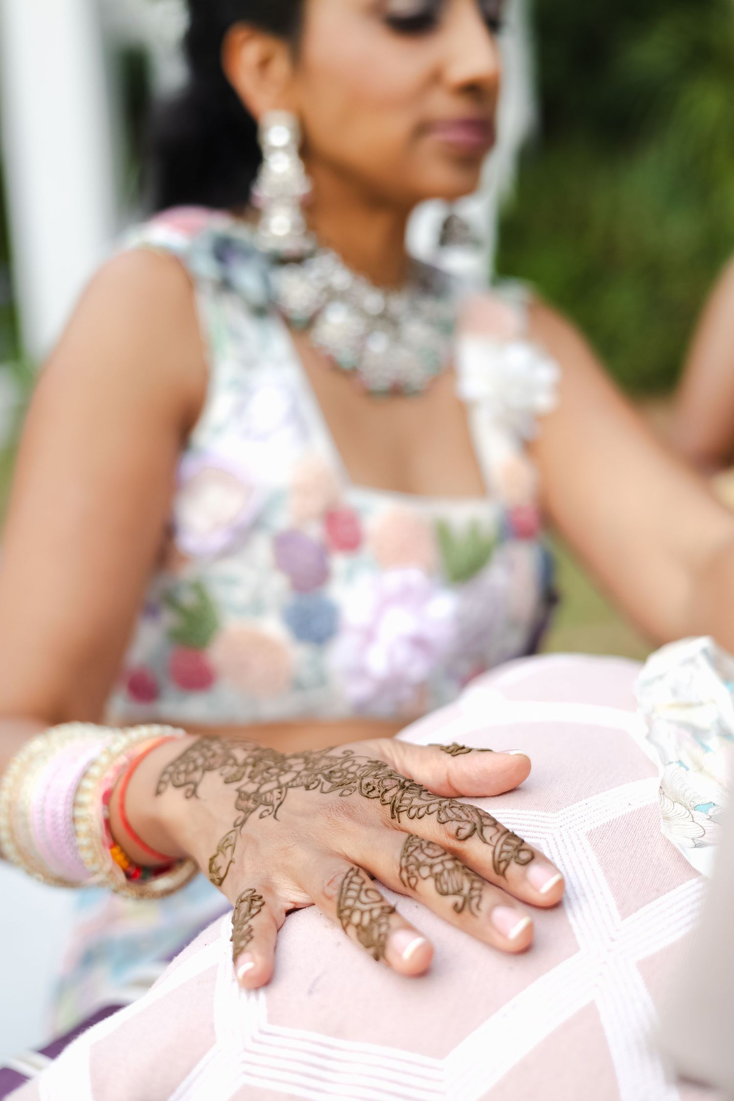 Hand adorned with intricate henna design and bangles rests on pink surface at traditional celebration event.