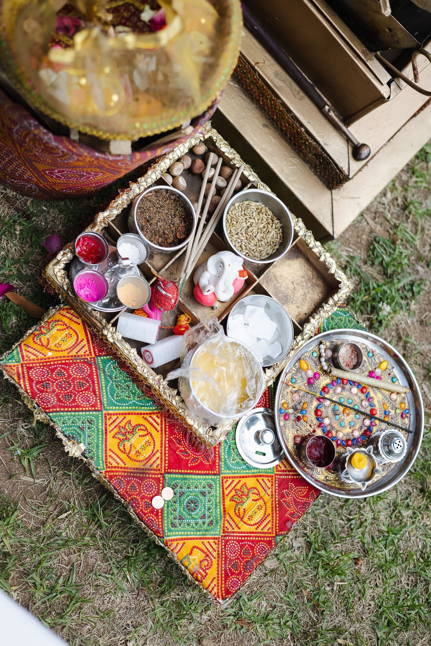 Traditional Indian puja ritual items and offerings arranged on a colorful patterned cloth with spices, flowers and ceremonial bowls.