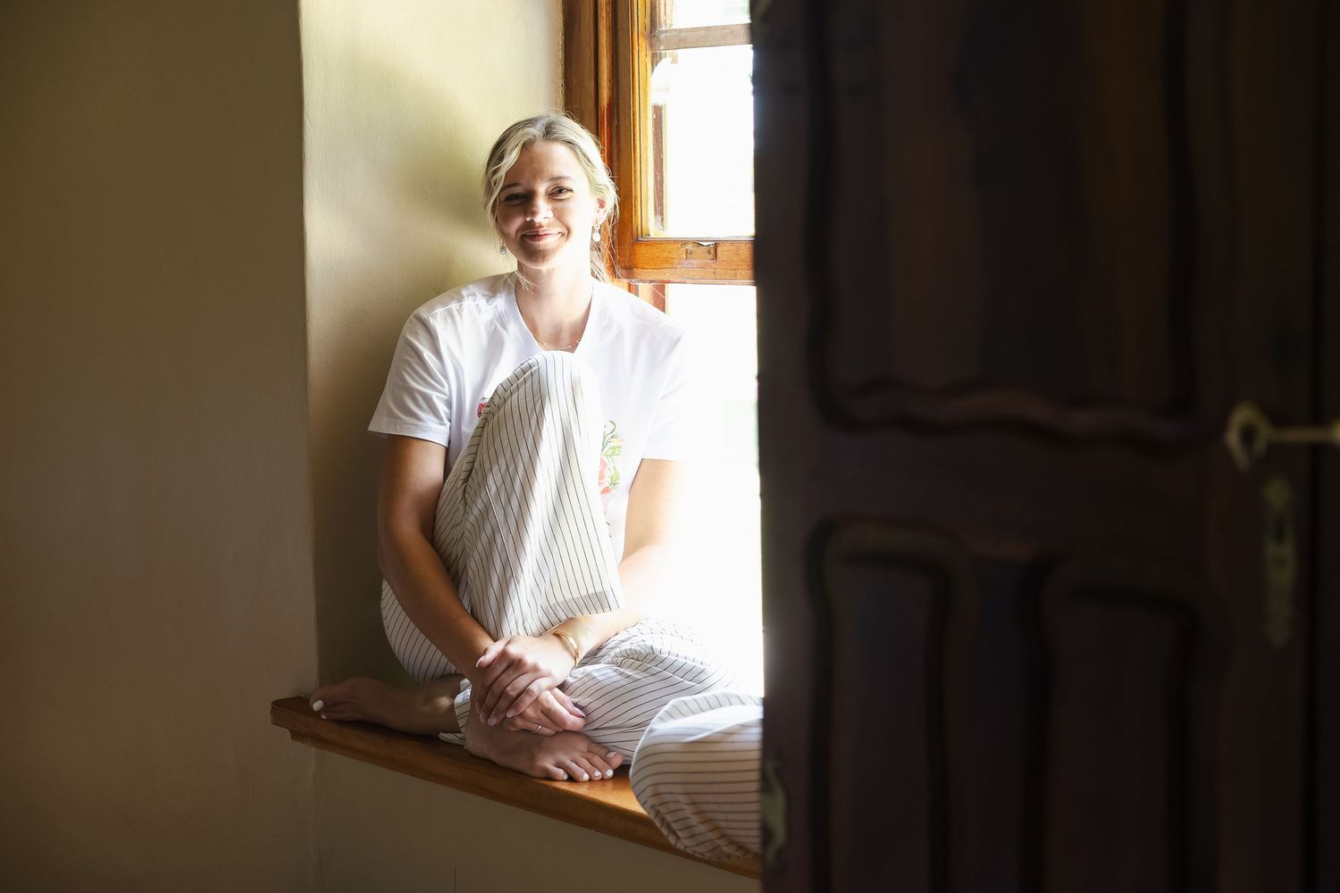Person in white shirt sitting by window with sunlight streaming in creating a warm, peaceful atmosphere.