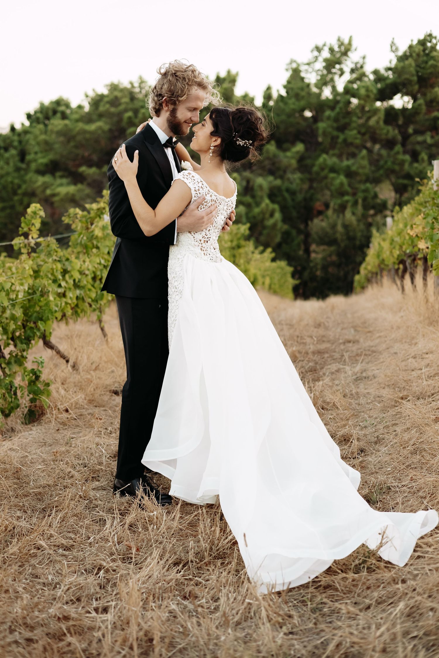 Dancing couple in formal wedding attire twirls in golden dry grass field.