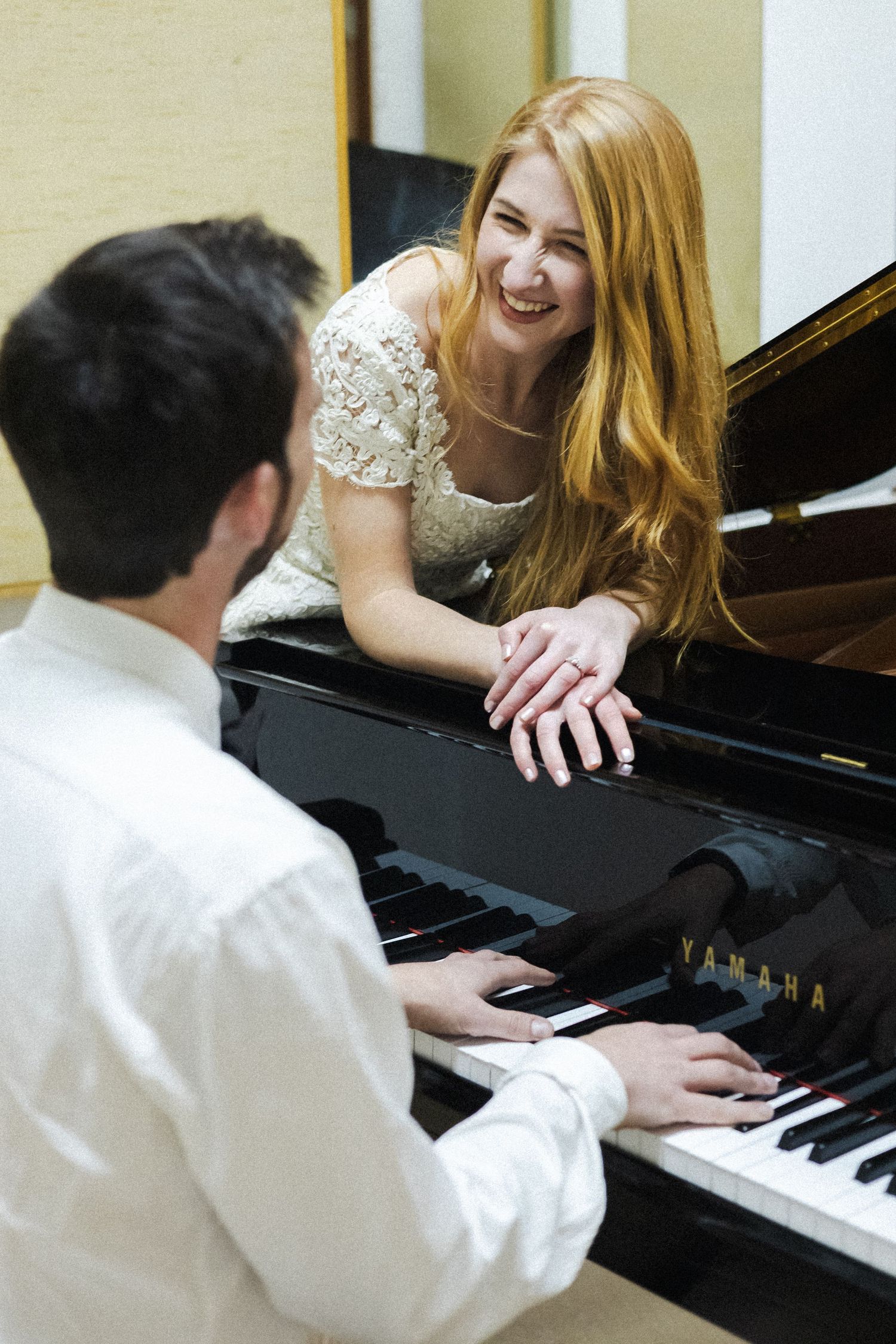 Two people share a joyful moment while sitting at a grand piano during a music lesson or performance.