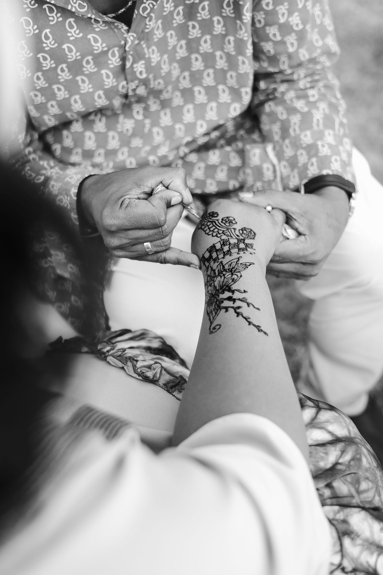 A sequence of black and white photos showing someone getting a delicate floral henna tattoo design on their arm.