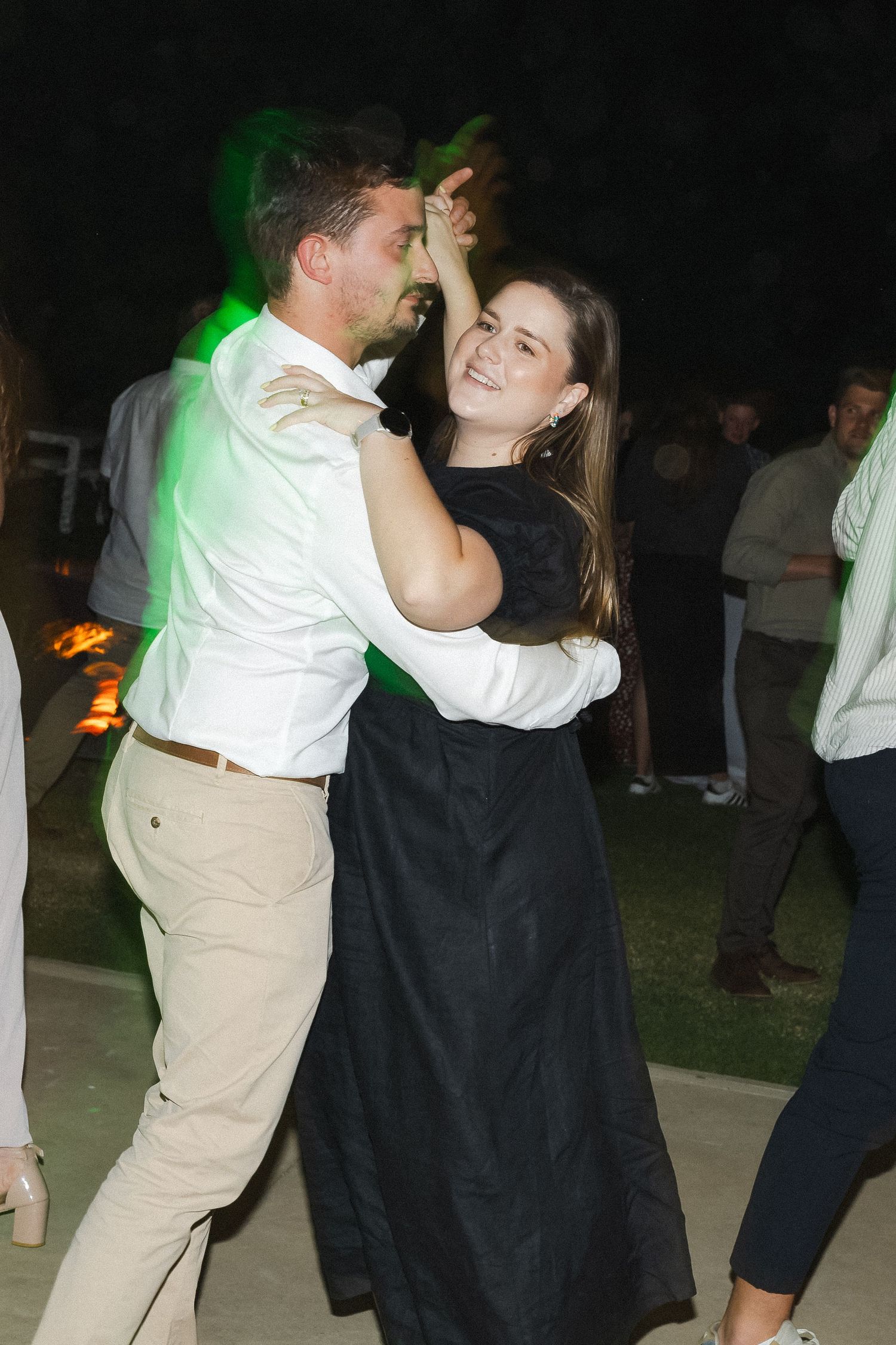 Couples dancing together at an evening event with colorful lighting in the background.