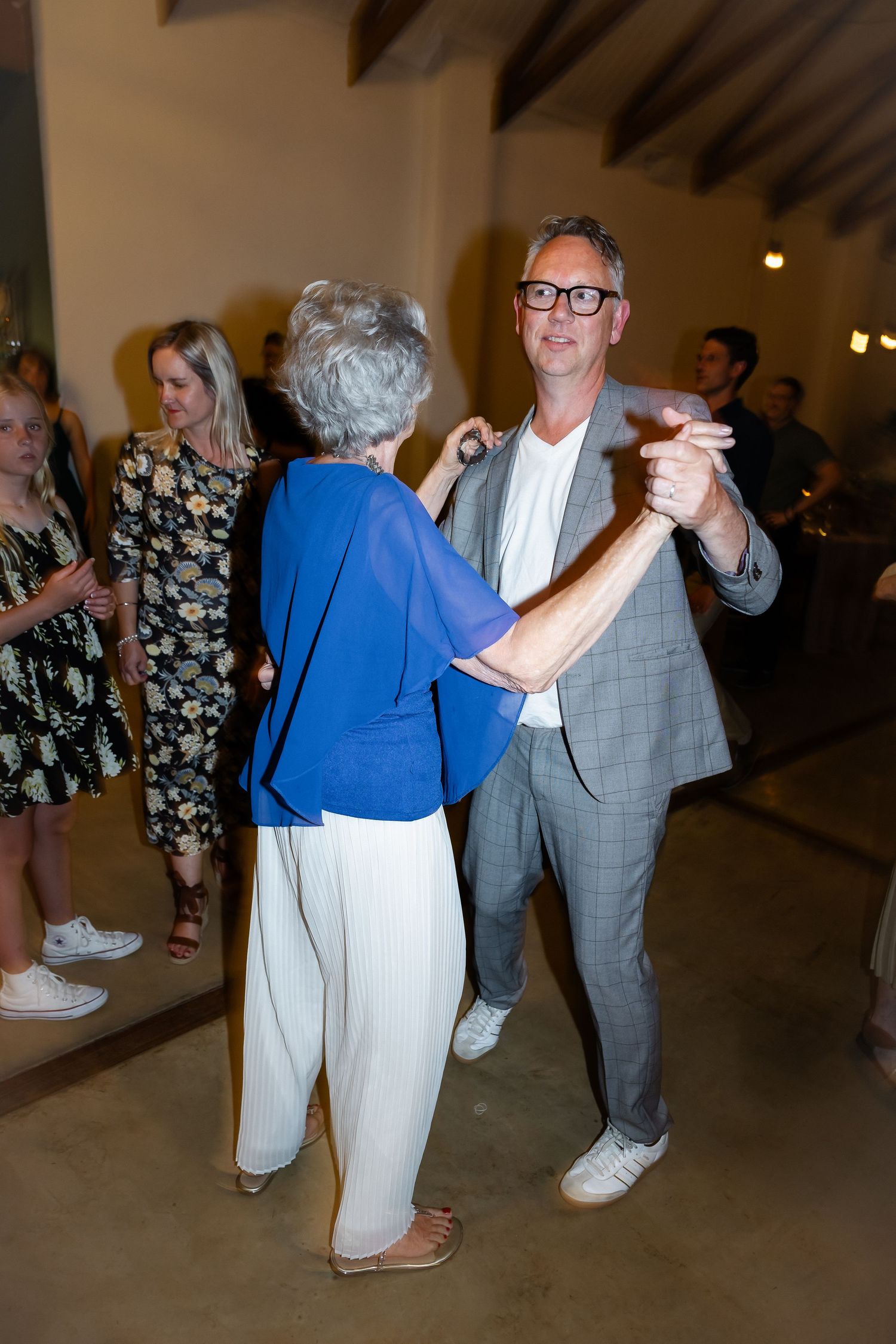 Wedding guests in formal attire dancing together under pendant lights.
