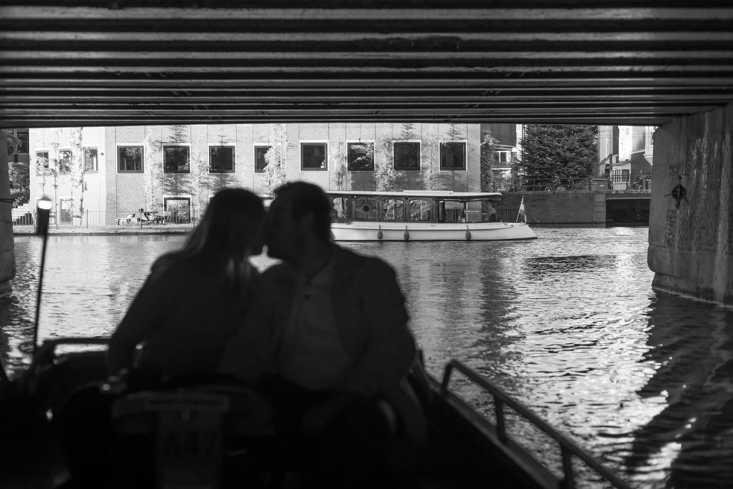 Silhouetted couple sitting together on a boat under a bridge on a calm urban canal in black and white.