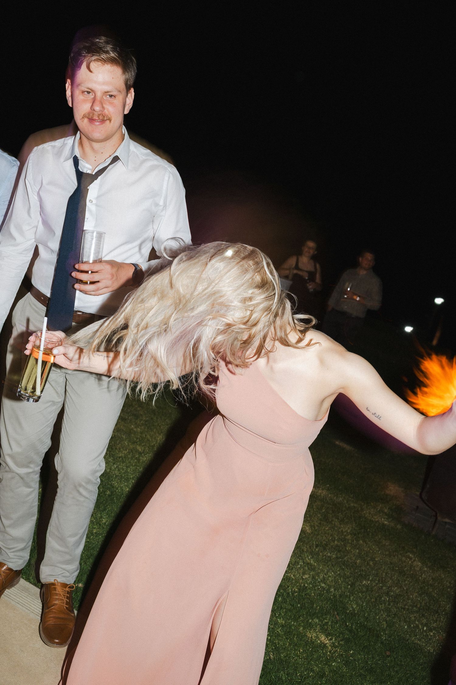 Party guests dancing and holding drinks during an outdoor evening celebration.