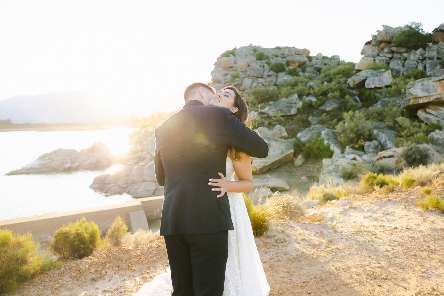 Silhouetted wedding couple embraces against stunning sunset and mountain landscape.