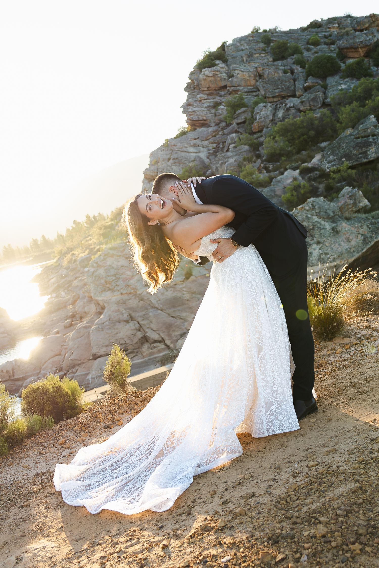 A romantic wedding couple embraces during sunset on a rocky cliff overlooking scenic mountain views.