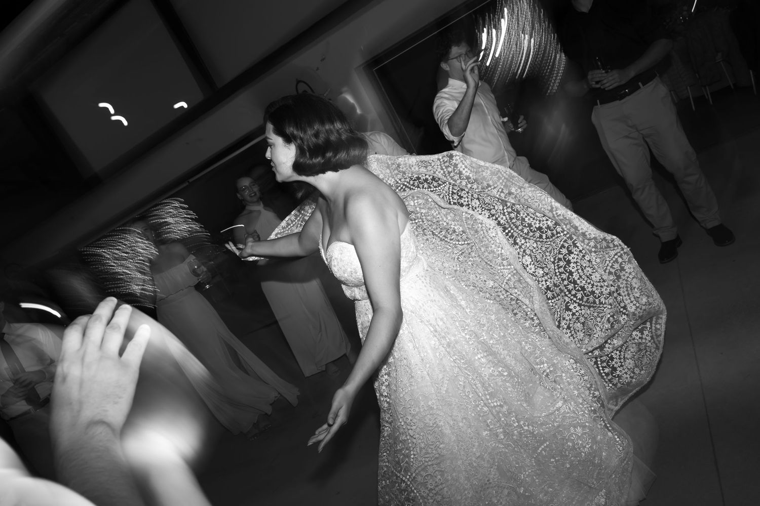 A bride in a white lace wedding dress walks down a dark hallway with dramatic lighting.