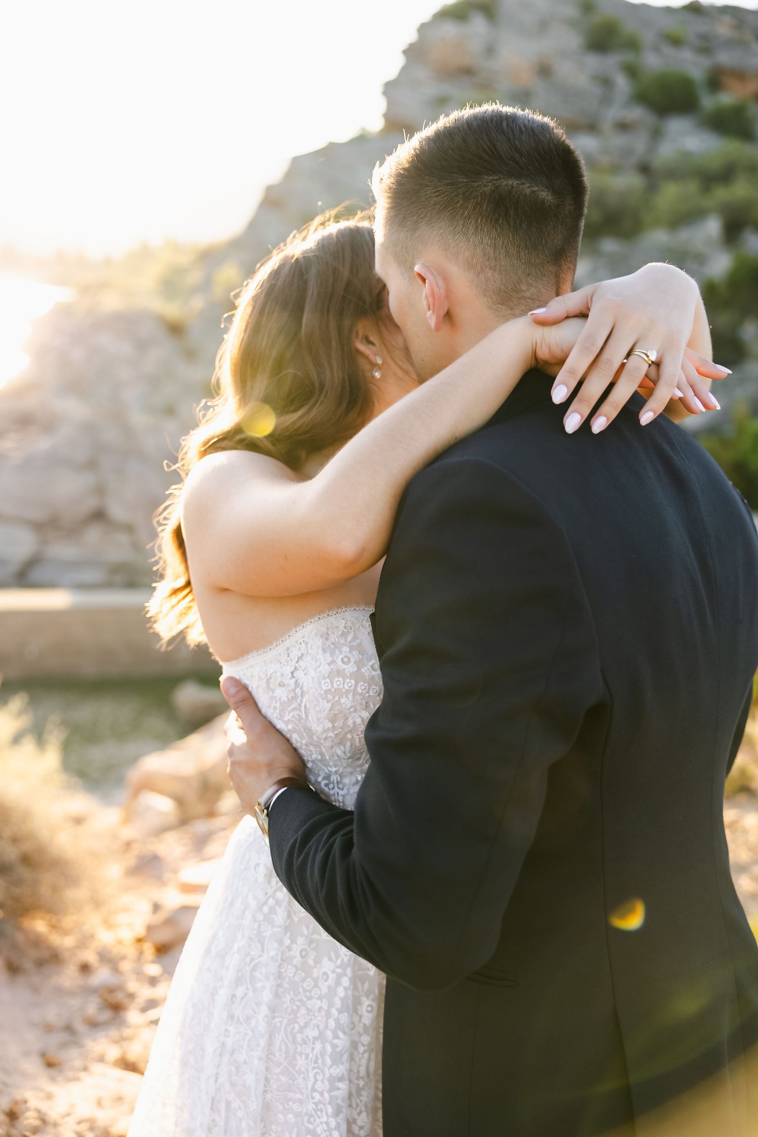 A tender embrace between newlyweds backlit by golden sunlight against rocky terrain.