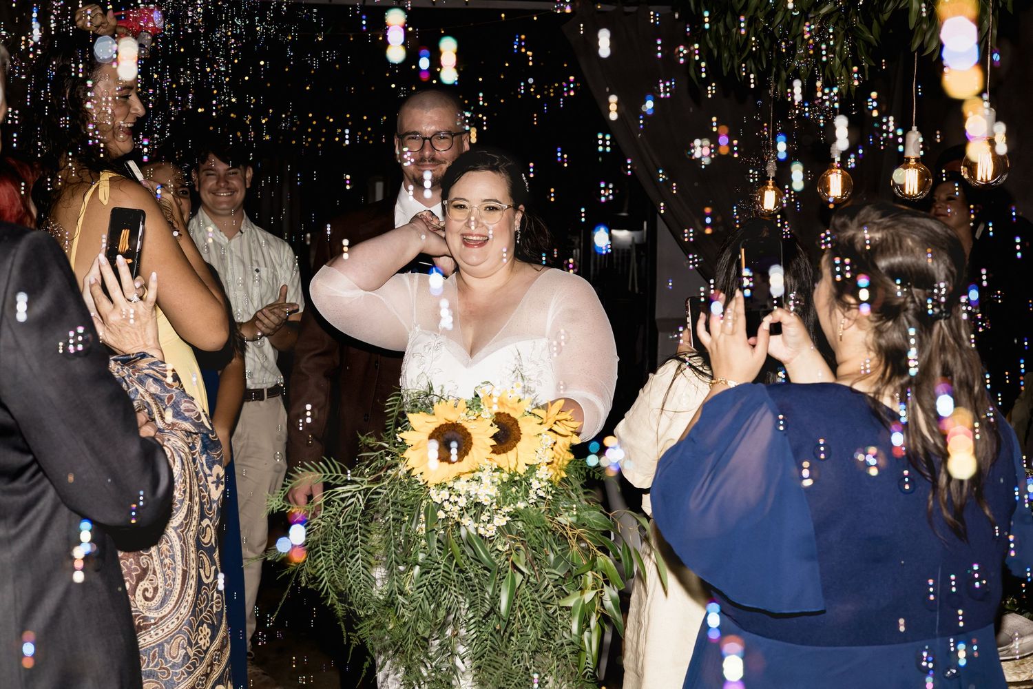 Bride with sunflower bouquet celebrates with guests at festive wedding reception.