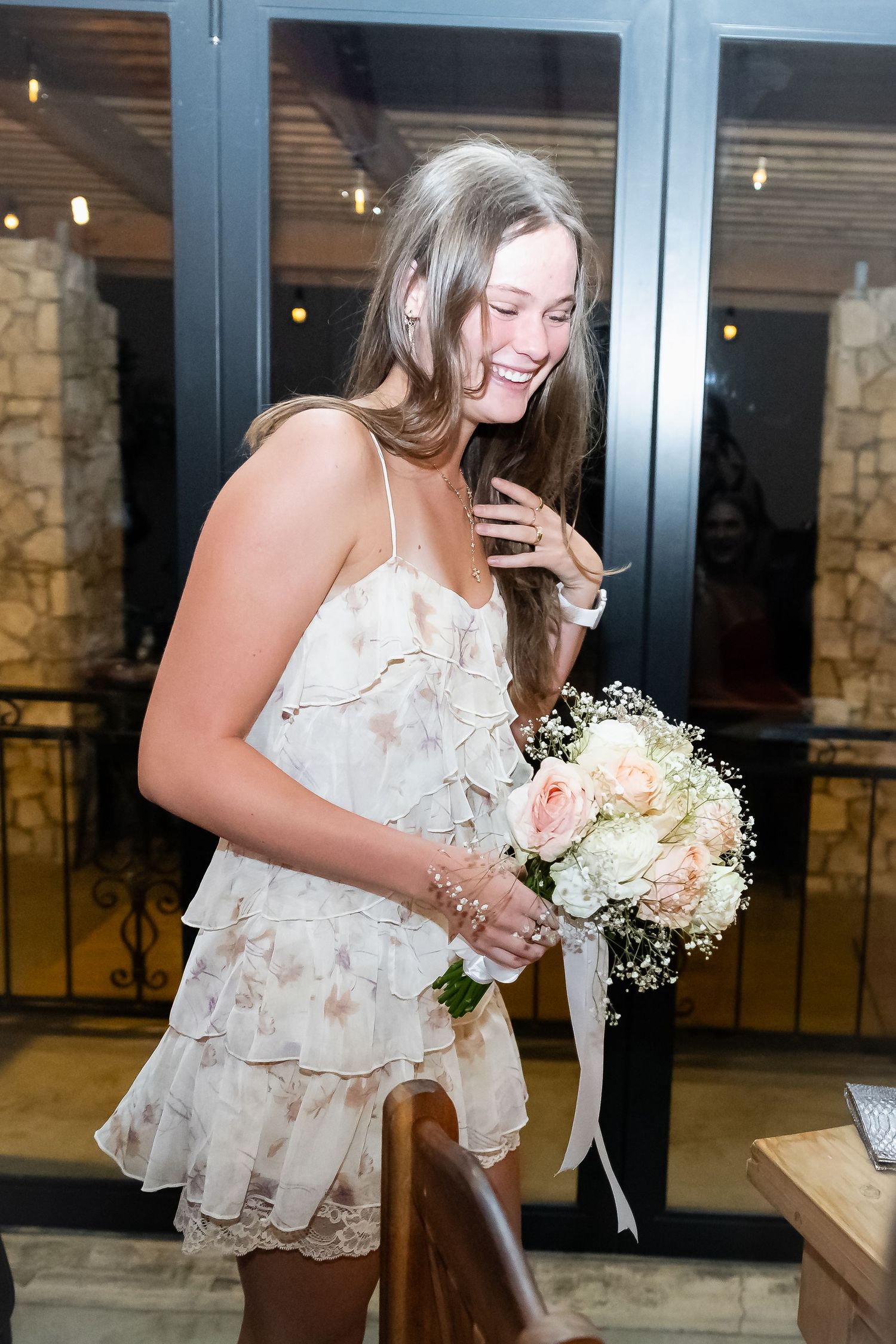 Bridesmaids in floral dresses share joyful moments while holding white bouquets at wedding celebration.