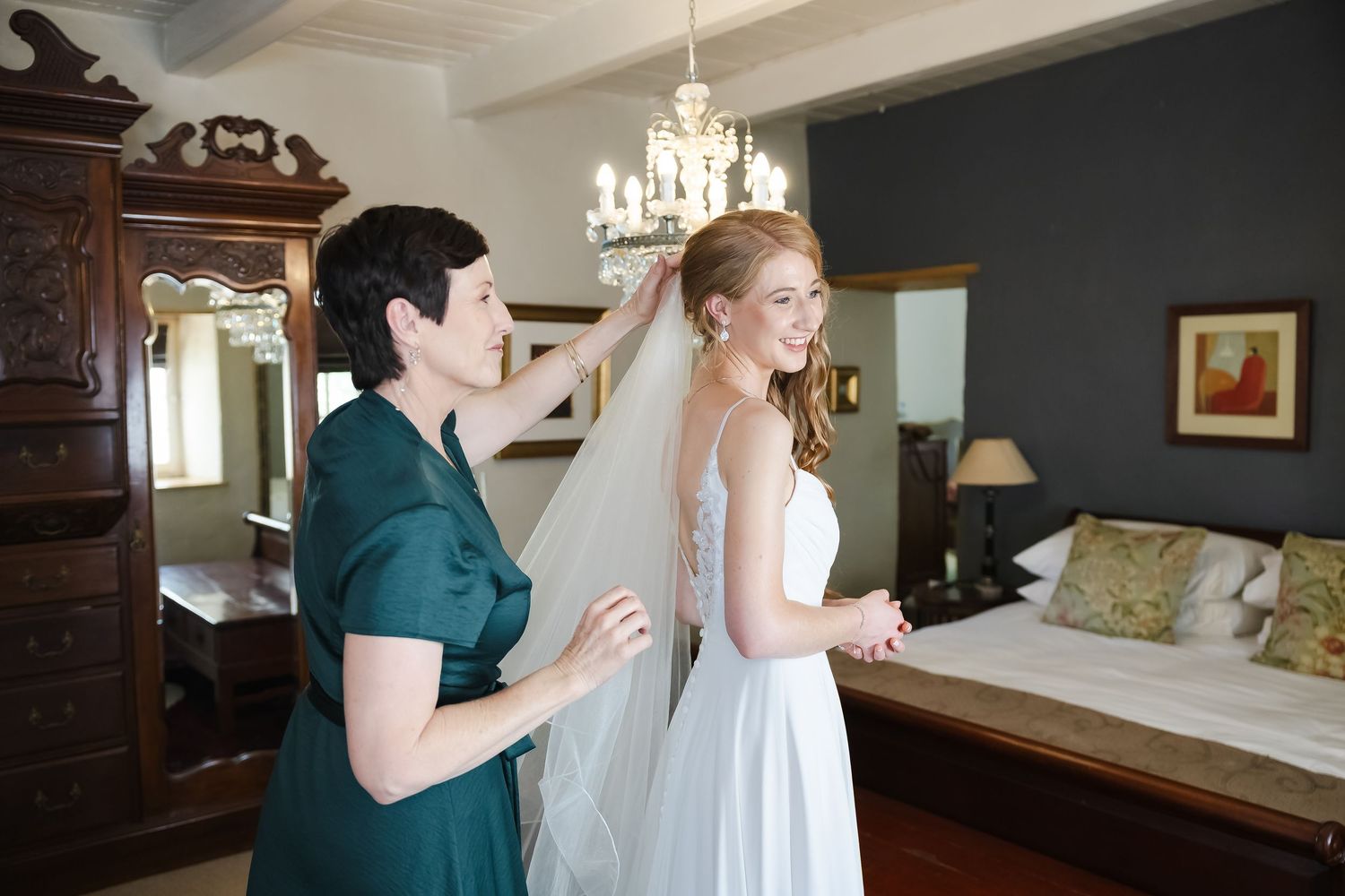 Wedding preparation scene with someone helping adjust the bride's dress in an elegant bedroom.
