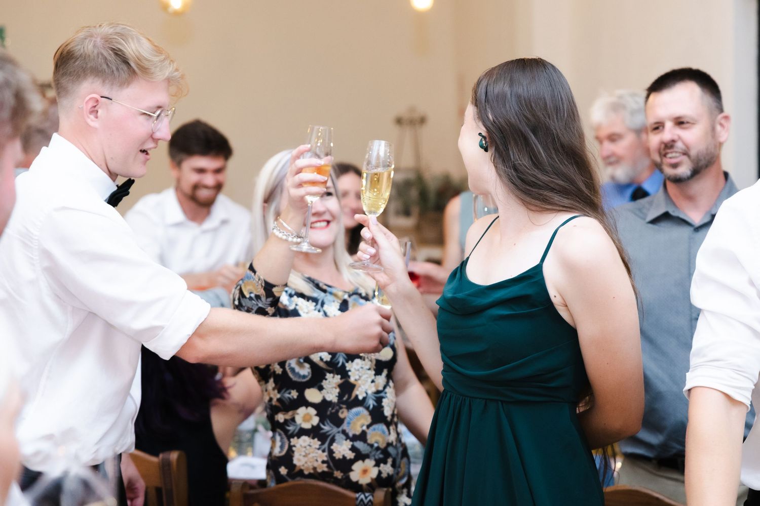 Wedding guests raise champagne glasses in celebration during an indoor reception.