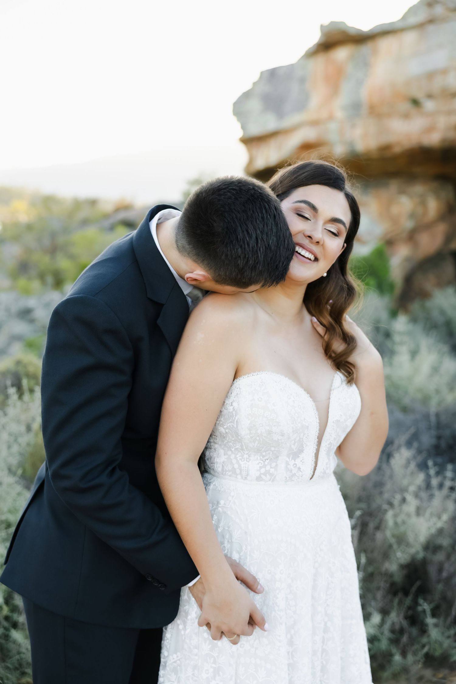A romantic wedding moment captured against a rocky desert backdrop during golden hour.