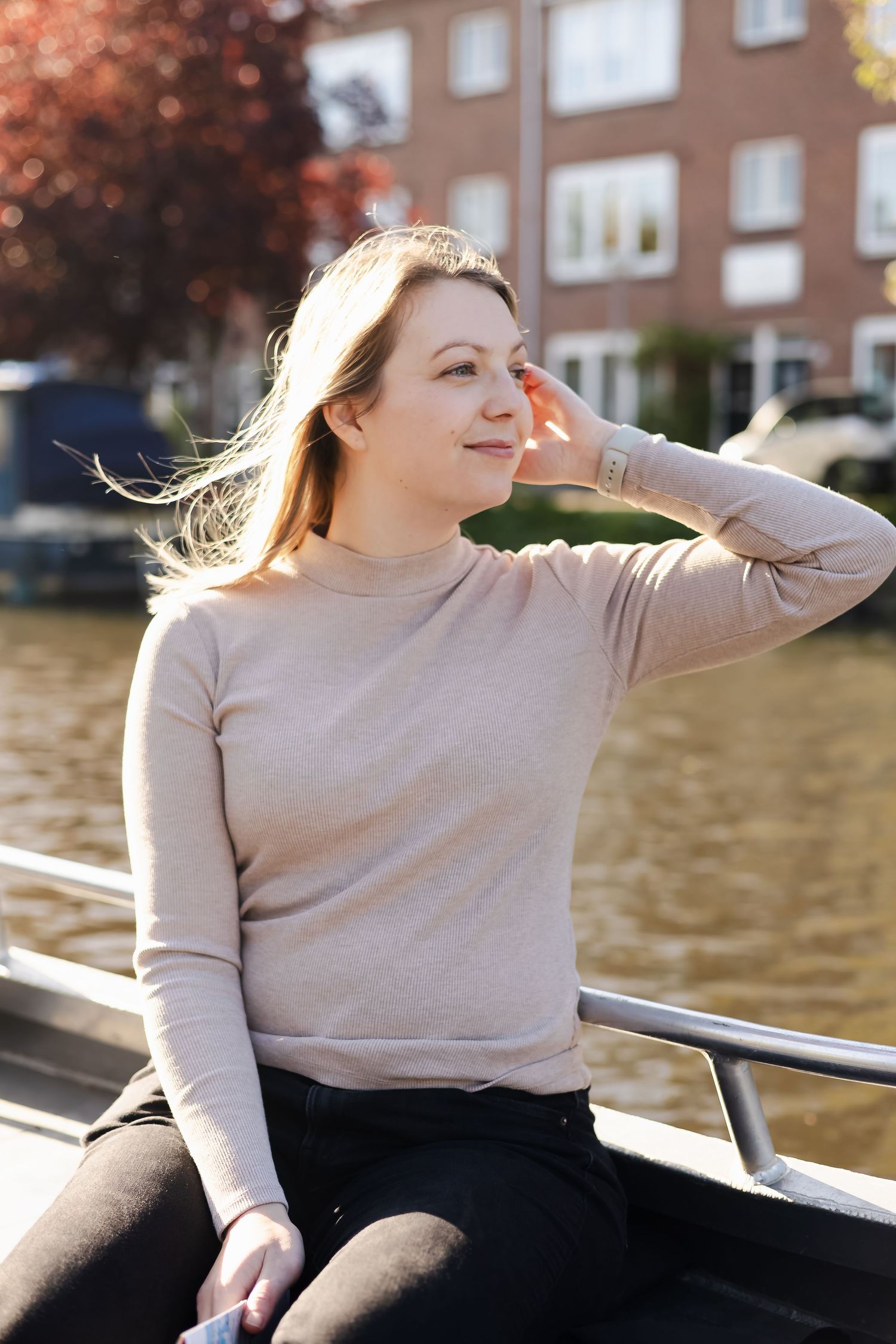 Young woman in beige sweater sitting on a boat, enjoying a sunny day on an Amsterdam canal.