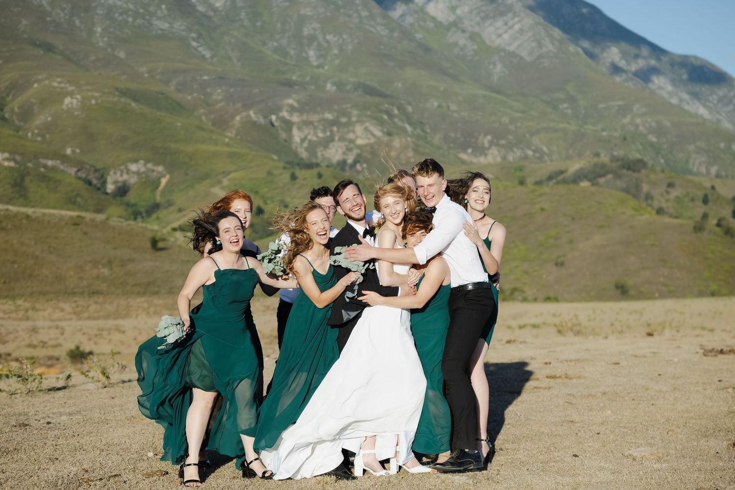 Wedding party poses playfully in a sequence of shots against a scenic mountain landscape backdrop.