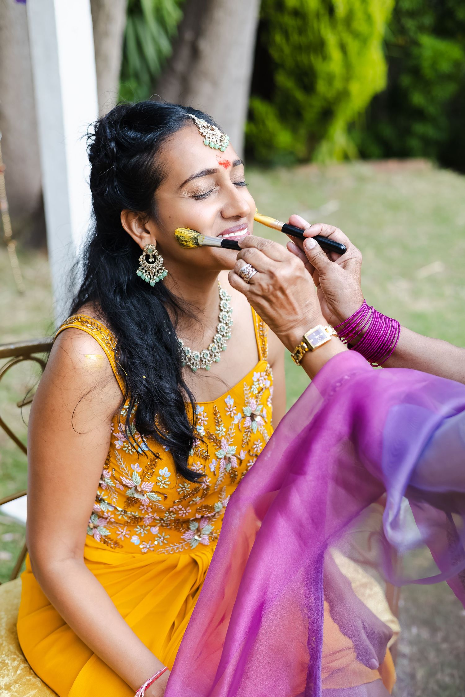 Close-up shots of turmeric application during a traditional Indian haldi ceremony with yellow and purple outfits.