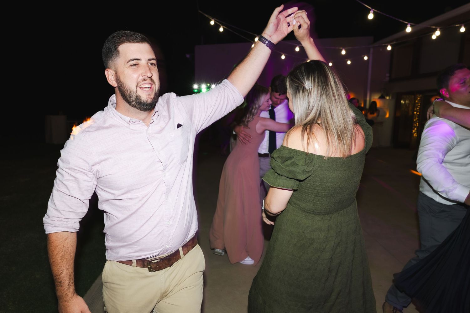 A couple dances together at an evening event with string lights visible in the background.